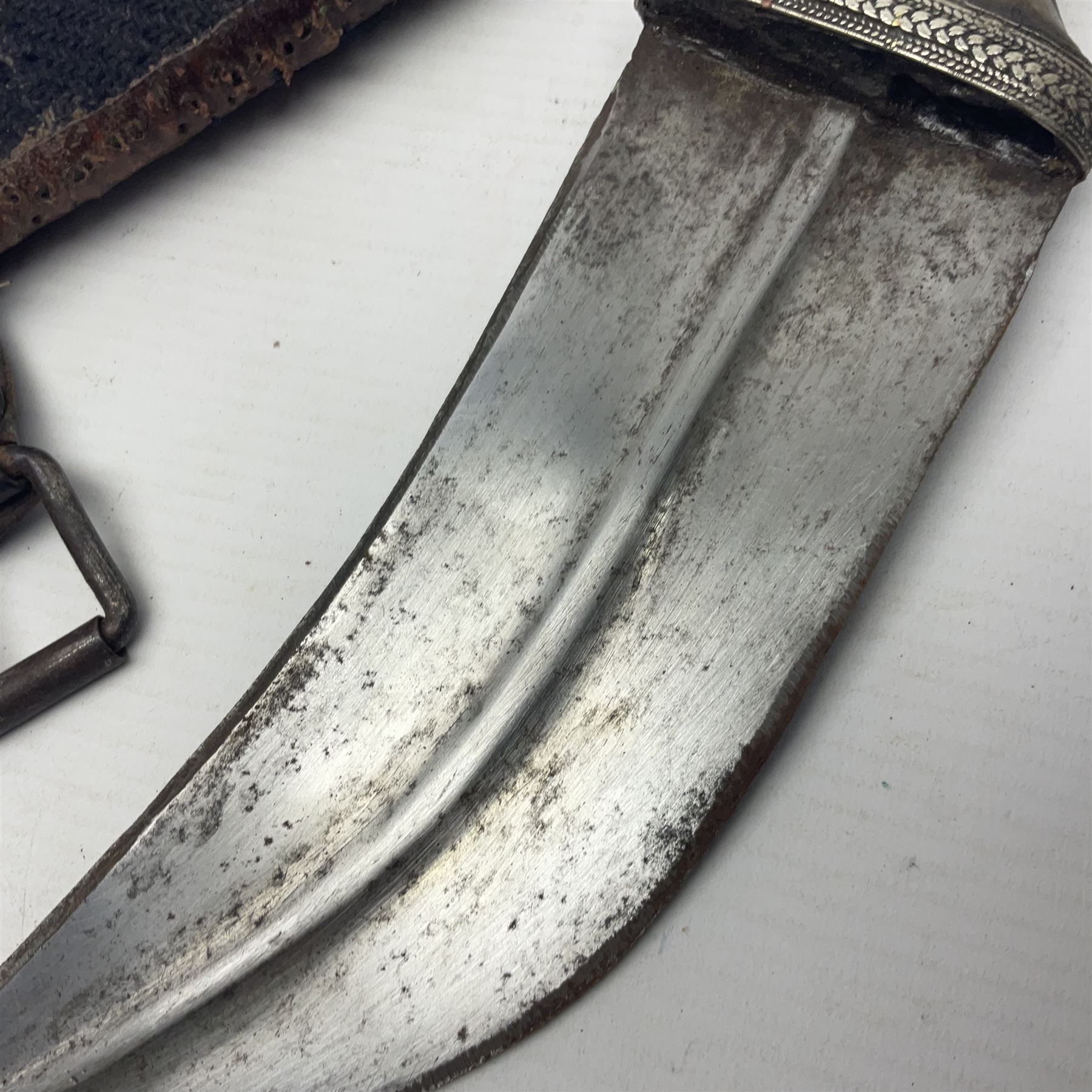 Eastern Jambiya, the 19cm double edge steel blade with raised medial ridge, waisted horn grip with pique work and white metal band; in stitched leather scabbard L33cm overall
