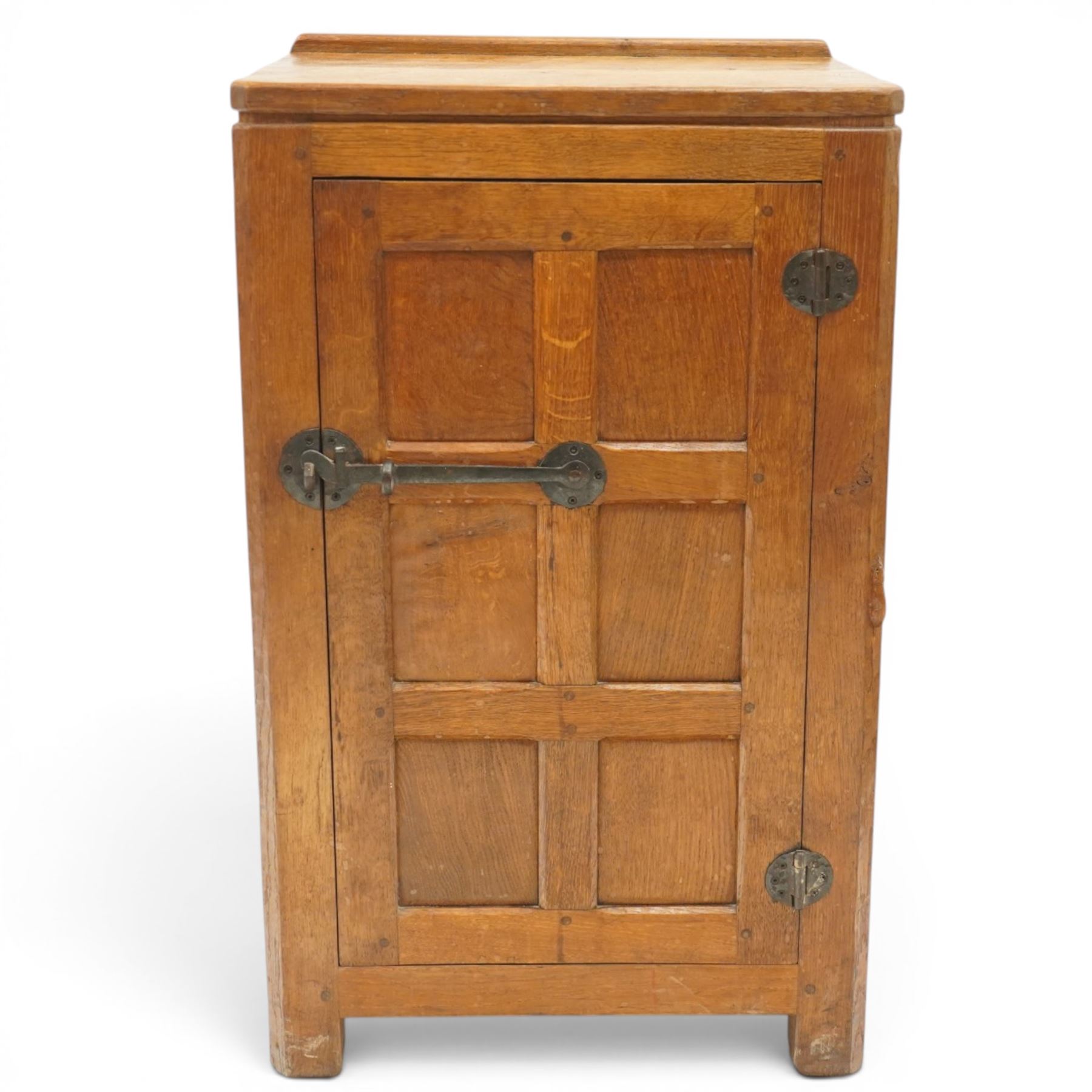 Mouseman - early-to-mid-20th century adzed and panelled dark oak bedside cupboard, raised back over rectangular canted top, fitted with single panelled cupboard door with chamfered rails and wrought iron fittings, enclosing two adjustable shelves, raised on canted square feet, carved with mouse signature, by the workshop of Robert Thompson of Kilburn