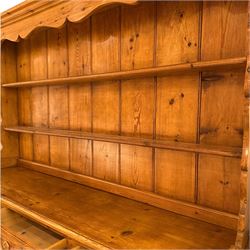 Late 20th century pine dresser, the plate rack with two fixed shelves and shaped apron over panelled back, base fitted with three drawers over two cupboard doors and central open niche flanked by turned uprights, on plinth base with shaped apron