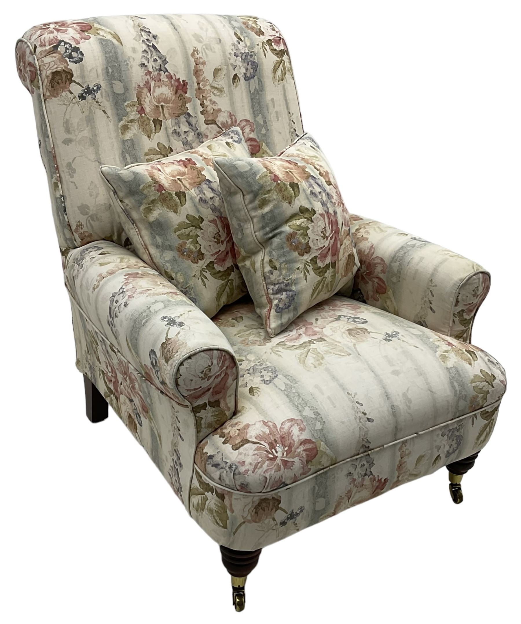 Victorian design armchair, rolled back and arms, upholstered in floral pattern fabric with two scatter cushions, on turned front feet with brass cups and castors