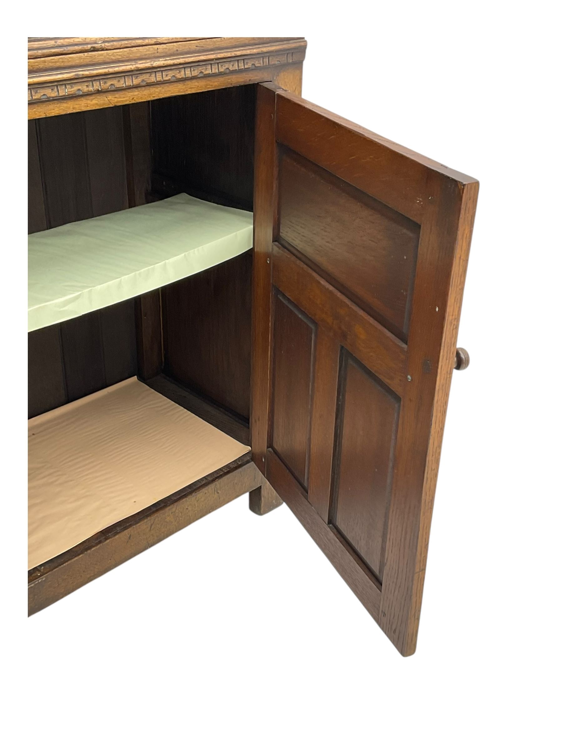 Jacobean design oak court cupboard, upper section with carved arched panelled cupboard door flanked by turned columns, beneath carved and moulded frieze, lower section fitted with two drawers over two cupboard doors with gothic arched panel decoration, raised on stile supports