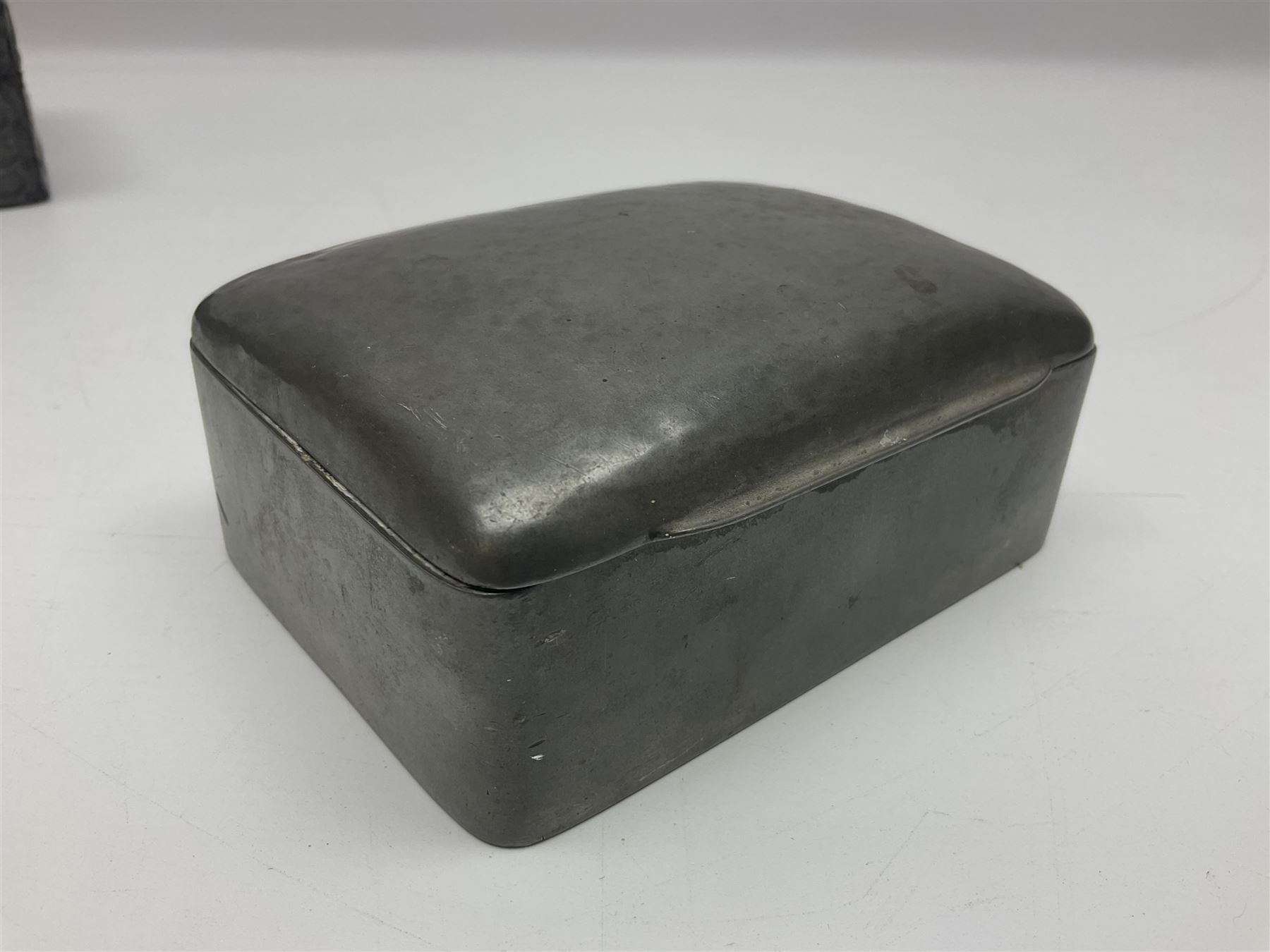 Liberty & Co Tudric pewter cigarette box, of plain rectangular form, with planished decoration to the slightly domed cover, opening to reveal a softwood interior, stamped Made in England 01234 Tudric Solkets beneath, together with another cigarette box, with applied pewter panels repousse decorated throughout with flower heads and leaves, with compartmentalised softwood interior, largest H5.5cm, W23cm