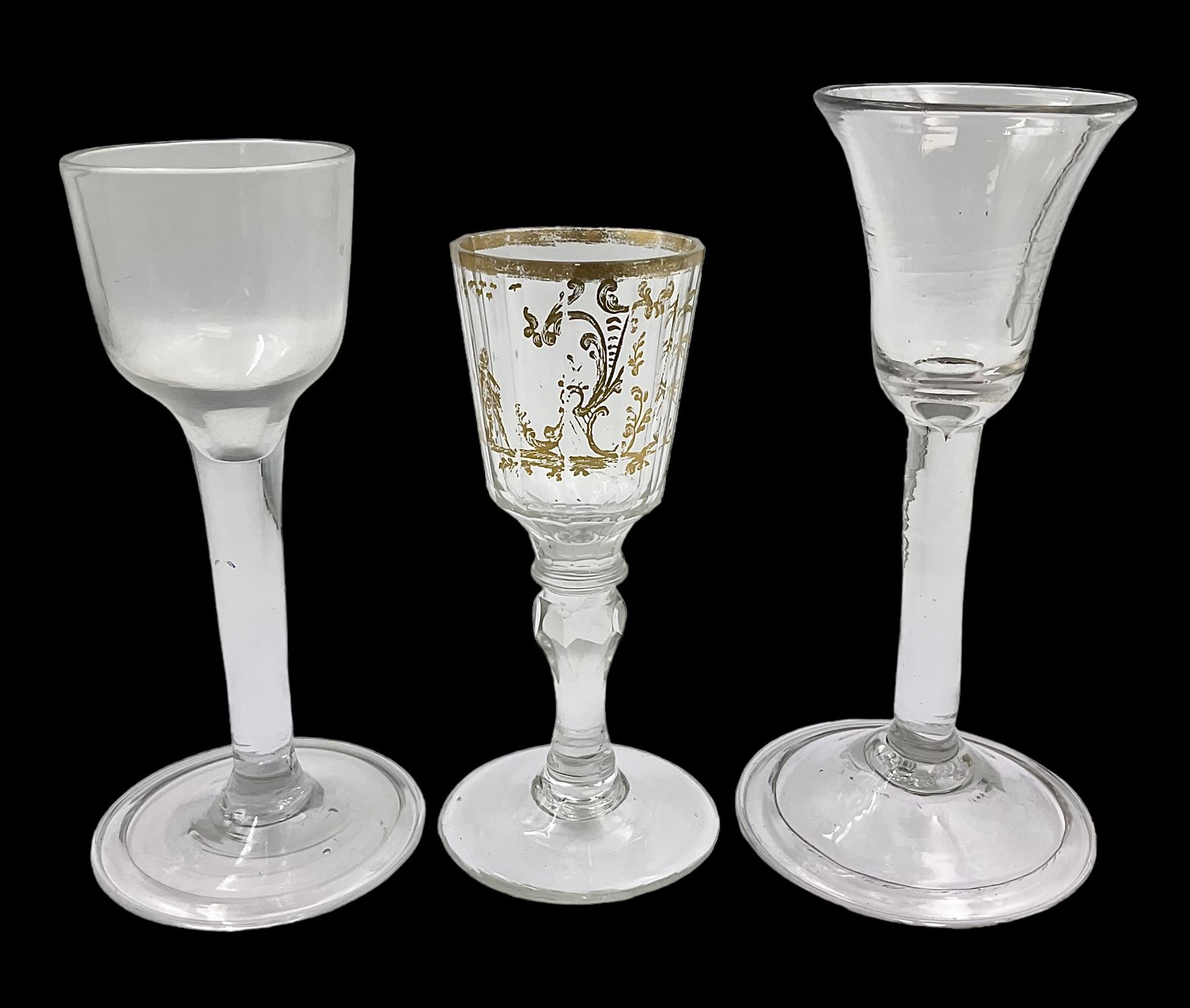 Three 18th century wine glasses comprising a plain stemmed glass with bell shaped bowl and conical folded foot H16cm, another plain stemmed glass with ogee bowl and folded foot and a Continental glass with gilt faceted bowl, decorated with male figure within a landscape, on a clear Silesian seven sided cut stem (3)