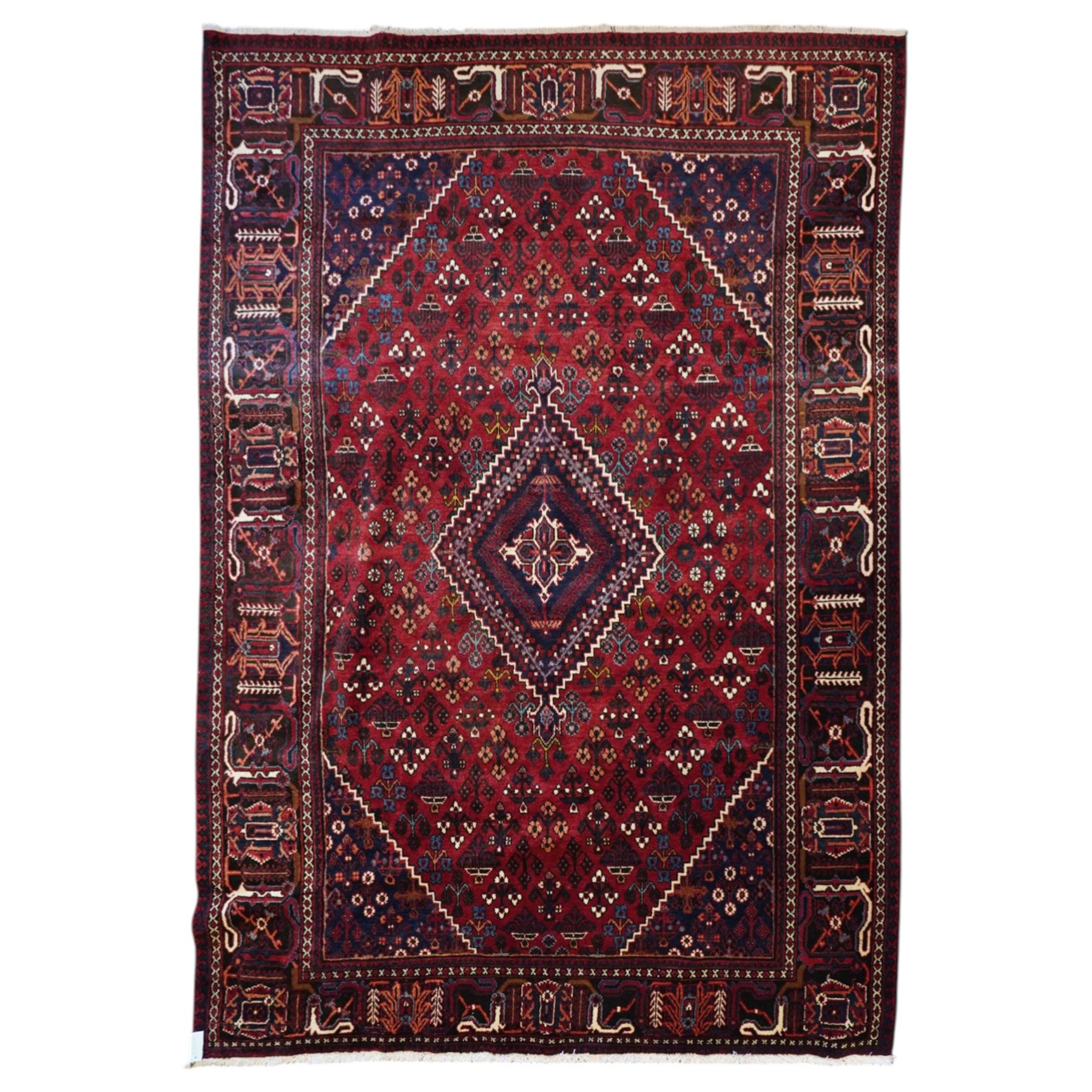 Central Persian Joshaghan hand-knotted carpet, deep red field decorated with a lattice design of stylized boteh and palmette motifs arranged around a stepped diamond medallion, navy corner spandrels similarly decorated enclosed by a dark indigo main border of floral and geometric motifs between multiple guard stripes, with cotton fringe ends 