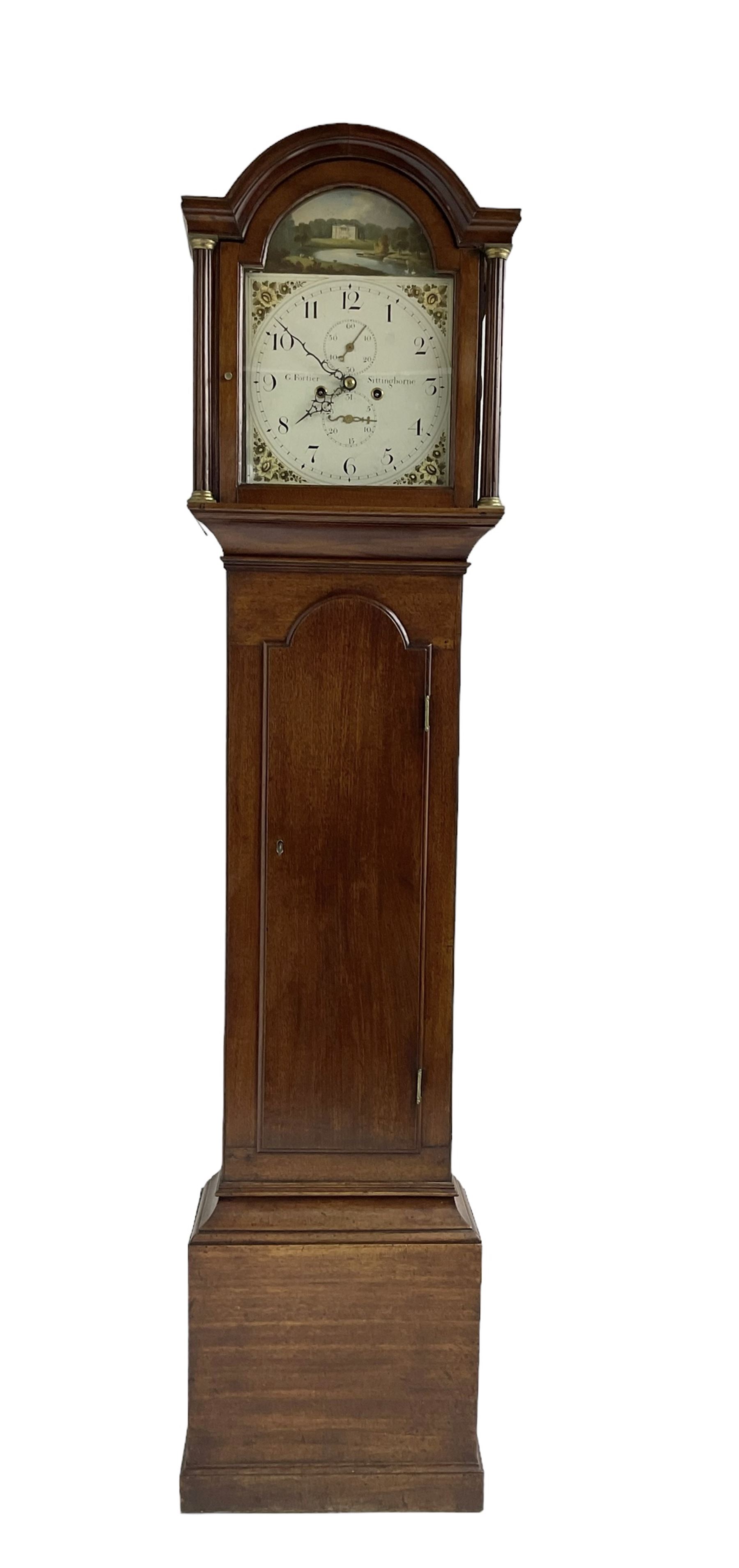 G Fortier of Sittingborn - Early 19th century 8-day mahogany longcase clock c1825, with a break arch pediment and hood door flanked by reeded pilasters with brass capitals, plain case with a long trunk door with a conforming break arch top, plinth with applied skirting, painted dial with upright Arabic numerals, date  and seconds dials, floral spandrels and a rural depiction of a country house and river to the arch, replacement steel hands with brass pointers to the calendar and seconds dials, dial pinned directly to a rack striking movement. With weights, pendulum and winding key.