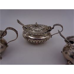 Three silver mustard pots with covers, comprising pair with acanthus capped handle, engraved initial to body and upon four paw feet, hallmarked Horton & Allday, Birmingham 1899, and an oval example with par fluted decoration throughout, hallmarks worn and indistinct, all with blue glass liners and matched hallmarked silver spoons