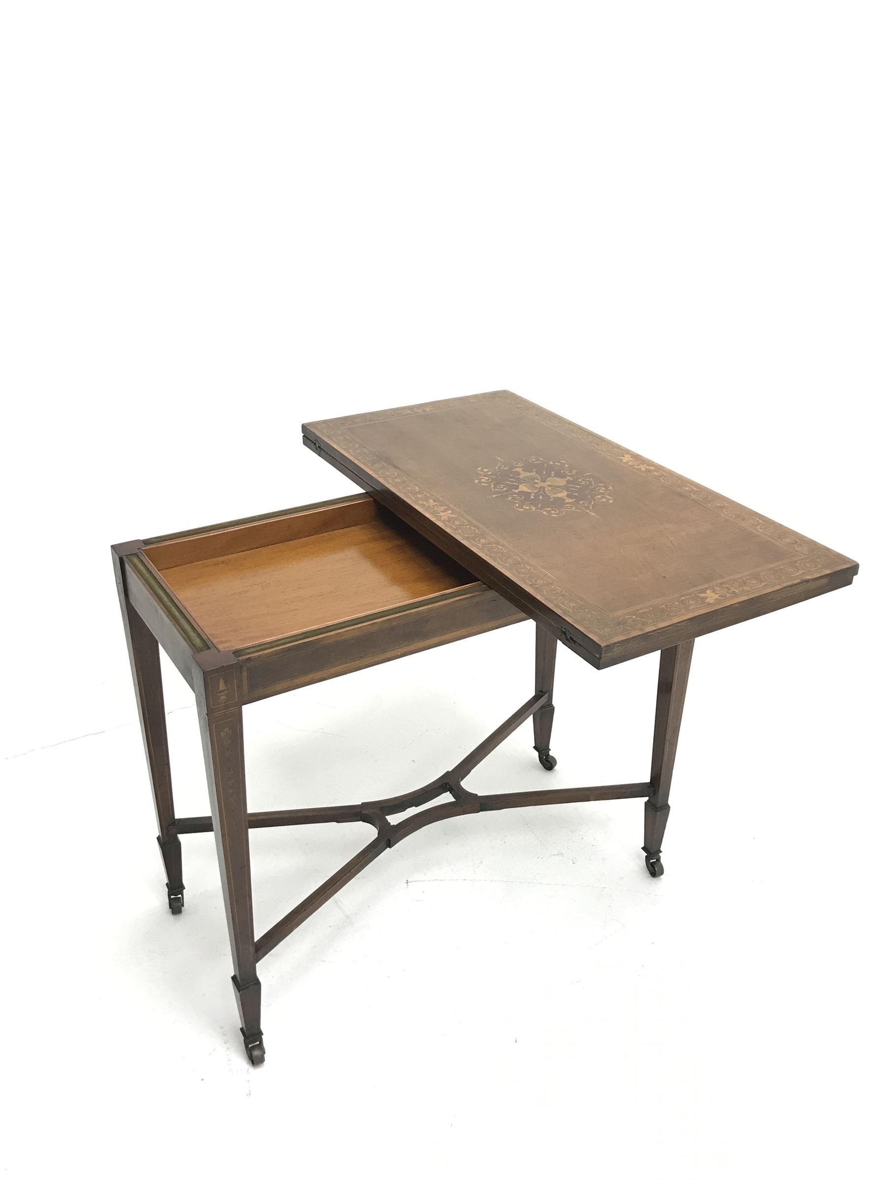 Edwardian walnut and mahogany Sheraton revival card table, rectangular top cross banded and inlaid with scrolling foliage, the central inlay with four urns and trailing leafage, swivel fold over action revealing storage well and baize lined interior, husk inlaid square tapering supports with spade feet, shaped and pierced x-framed stretcher, brass castors