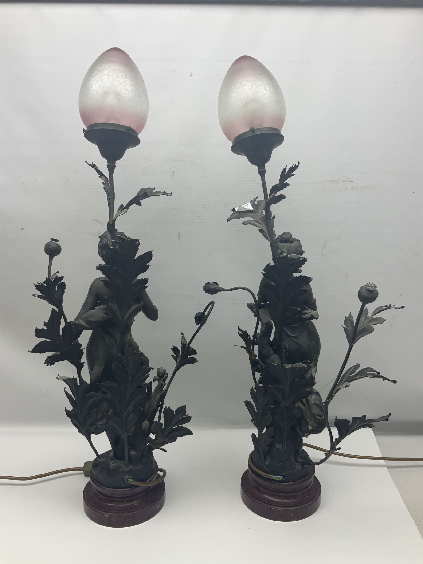 Pair of Art Nouveau style spelter figural table lamps, each mounted on rouge marble effect circular bases, with toleware flower heads and leafy decoration surrounding a female figure, H90cm