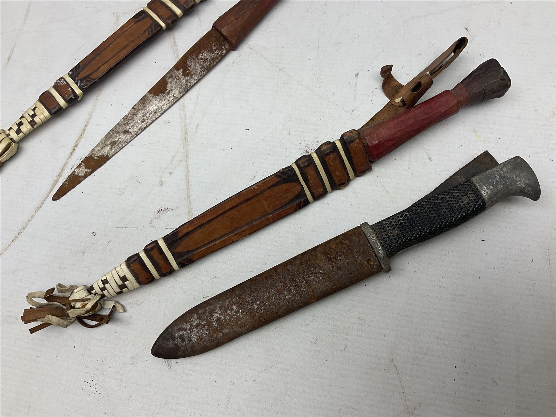 Indian kukri with 29cm curving steel blade and nickel mounted horn grip; in leather covered scabbard with one skinning knife L42cm overall; Hitler Youth knife with scabbard in relic condition; and three African graduated knives each with crudely carved wooden grips and painted leather covered scabbards (5)