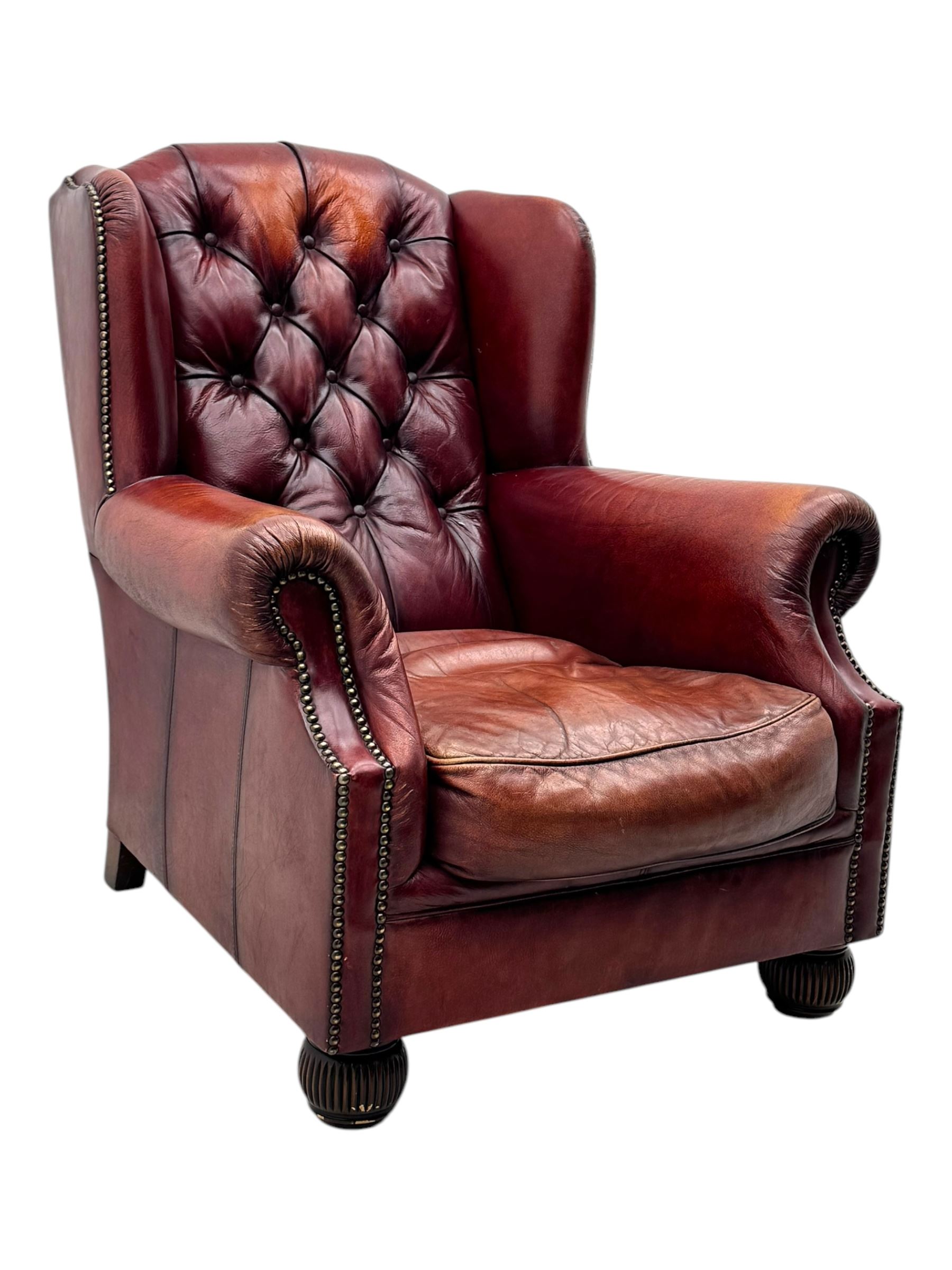 Tetrad - pair of 'Oskar' wingback armchairs, deep-buttoned oxblood leather upholstery with rolled arms and brass stud trim, raised on turned and reed moulded feet
