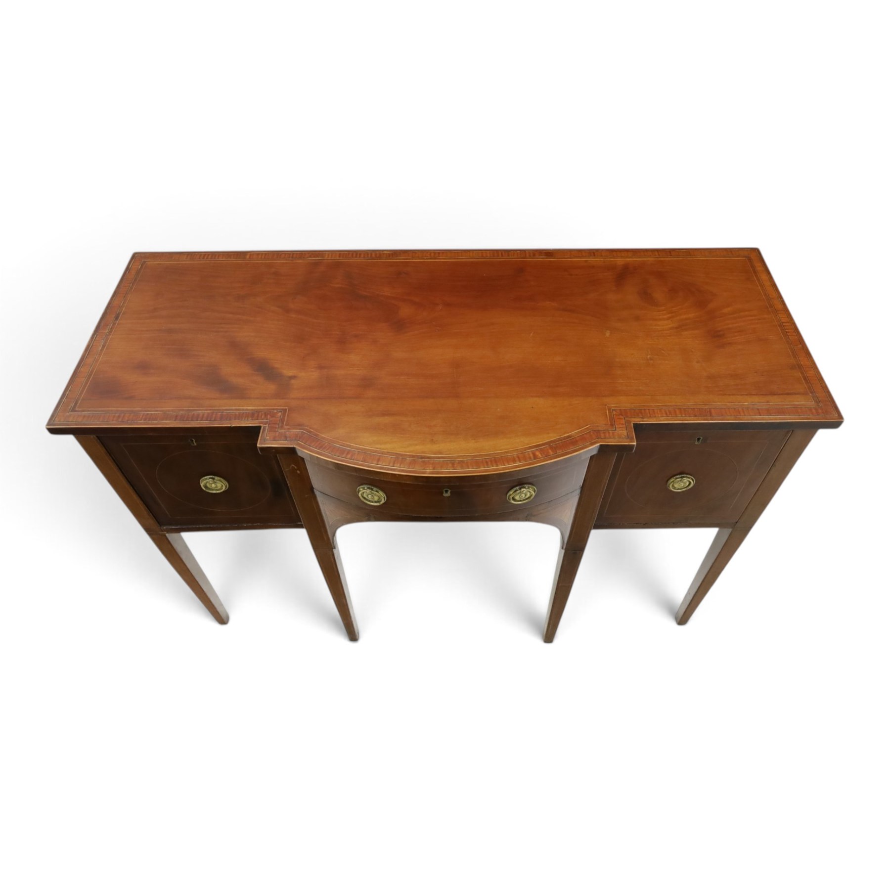 Regency period inlaid mahogany bow-breakfront sideboard, shaped rectangular top with crossbanding and ebony stringing, central convex frieze drawer flanked by cupboard and cellarette drawer, over fan-inlaid spandrels, raised on square tapering supports