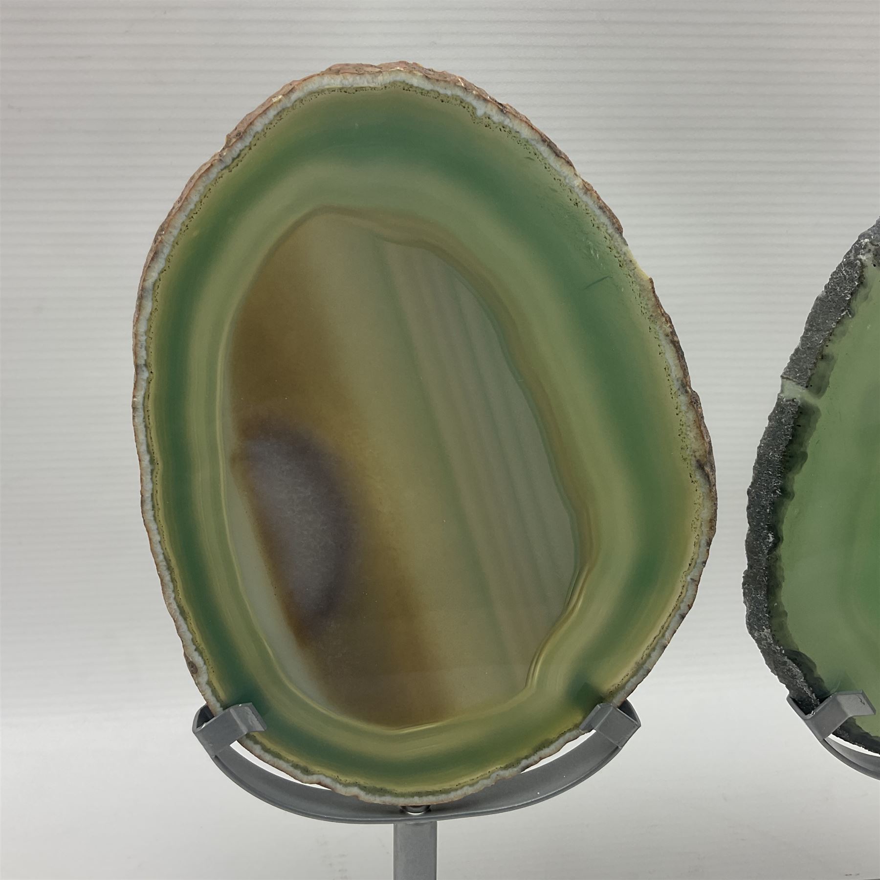 Pair of green agate slices, polished with rough edges raised upon silvered metal stands, H19cm