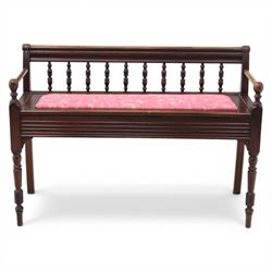 Early 20th century mahogany hall bench, spindle turned back with shaped top rail and open arms terminating in ball finials, upholstered seat within a fluted frieze, raised on turned tapering supports