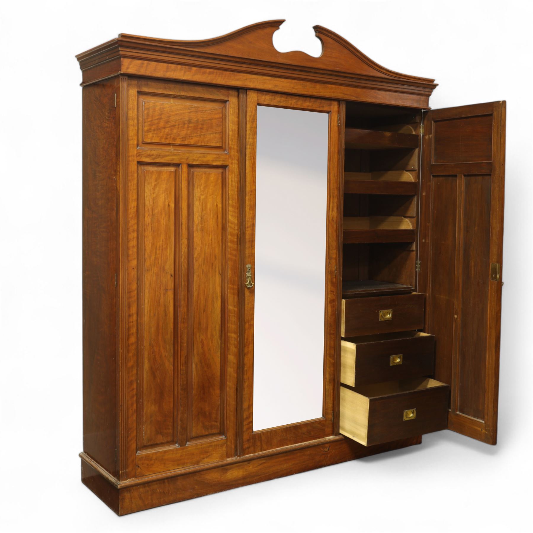 Edwardian walnut triple wardrobe, shaped broken-arch pediment over three doors comprising central mirrored door flanked by moulded raised and fielded panelled doors, interior fitted with hanging space and a bank of three open drawers above three brass recessed-pull drawers, on moulded plinth base