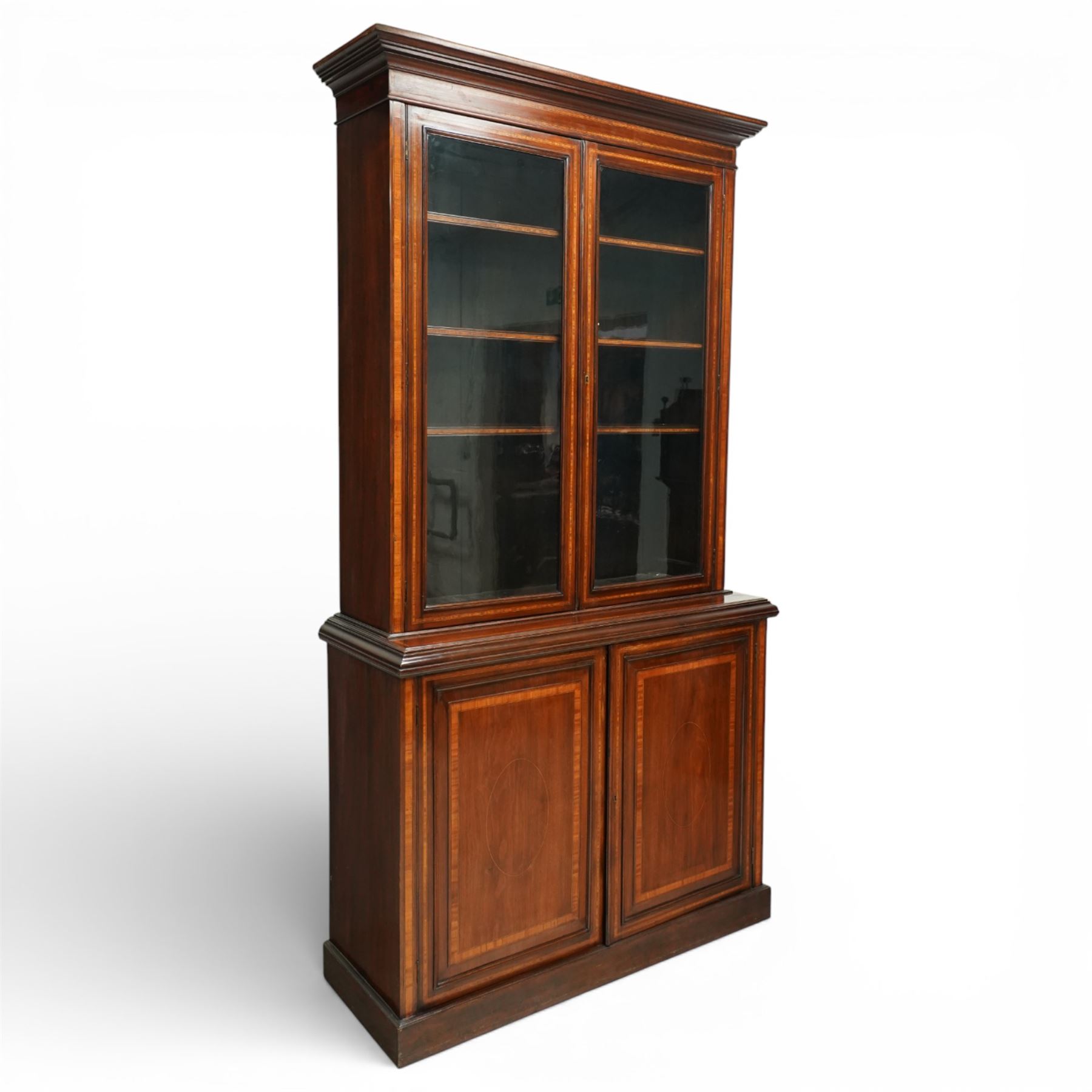 Large Edwardian walnut and satinwood enclosed bookcase-on-cupboard, projecting cornice over two glazed doors with satinwood and ebony banding and stringing enclosing three adjustable shelves, over two panelled doors enclosing two drawers above shelf, on skirted base
