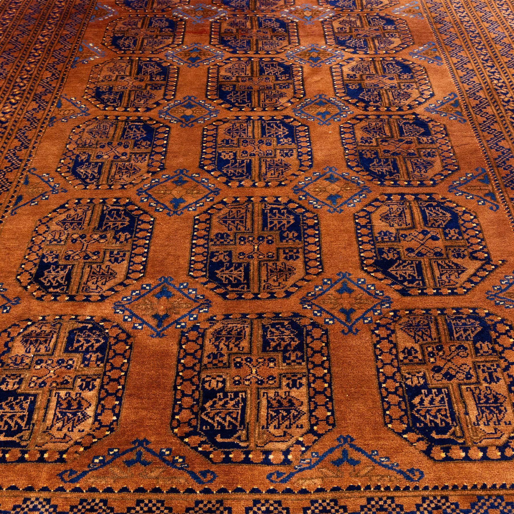 Pakistani Bokhara hand-knotted carpet, camel field decorated with rows of large tekke style octagonal guls enclosing stylized geometric motifs, interspersed with small stepped diamond devices within multiple geometric borders, with fringe ends 