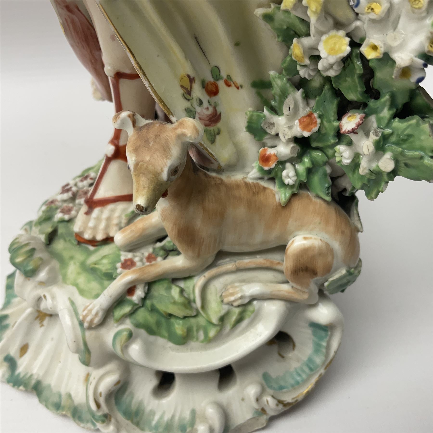 18th century Derby figure of Diana the huntress, circa 1760, modelled reaching for an arrow from quiver across her back, with recumbent hound at her feet, upon a scrolled base with bocage detail, H27.5cm