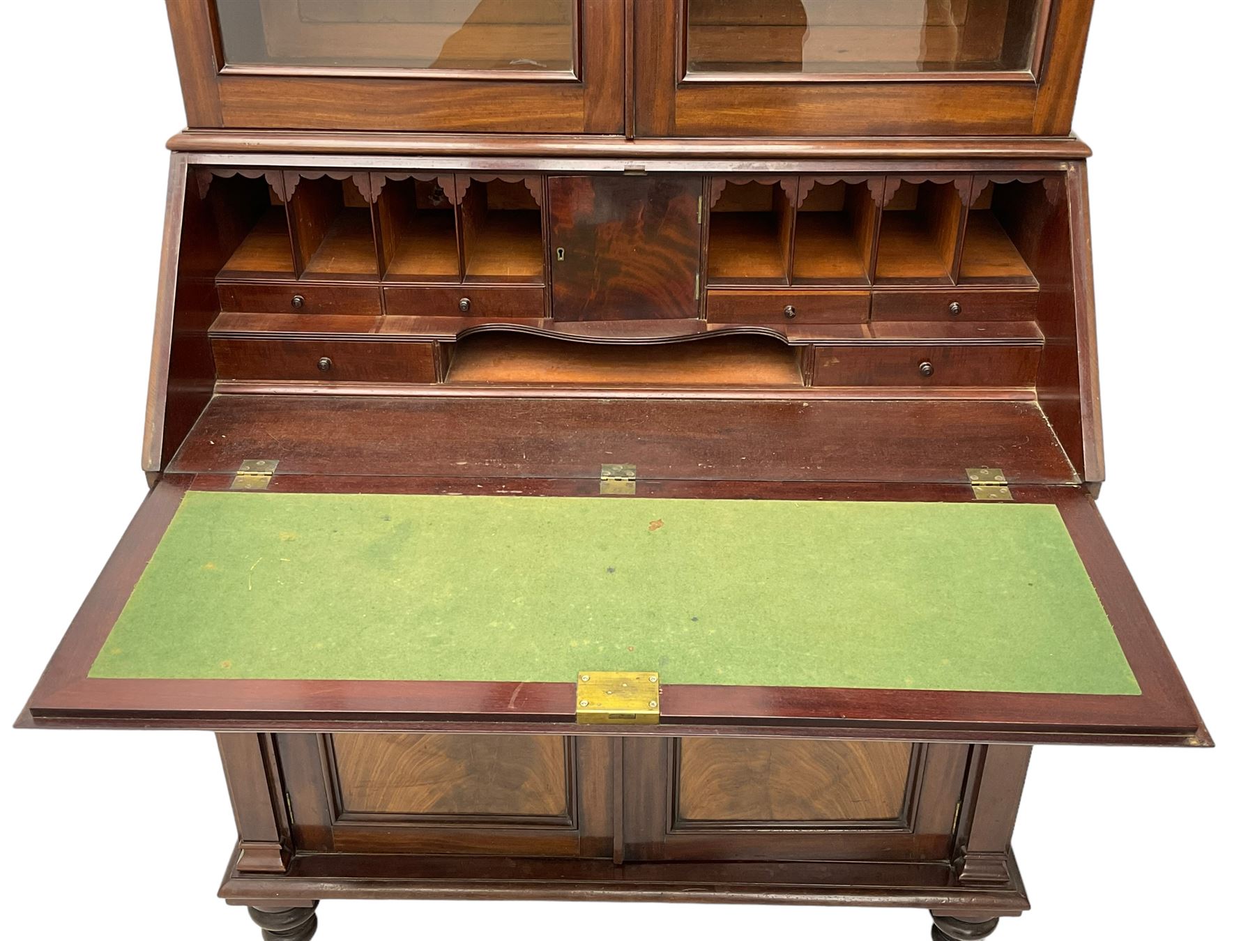Early 19th century figured mahogany bureau bookcase, projecting splay moulded cornice over three adjustable shelves enclosed by two glazed doors, fall front revealing pigeonholes, cupboard and drawers, pull-out strays with scroll carved terminals, double cupboard with two panelled doors, on turned feet 