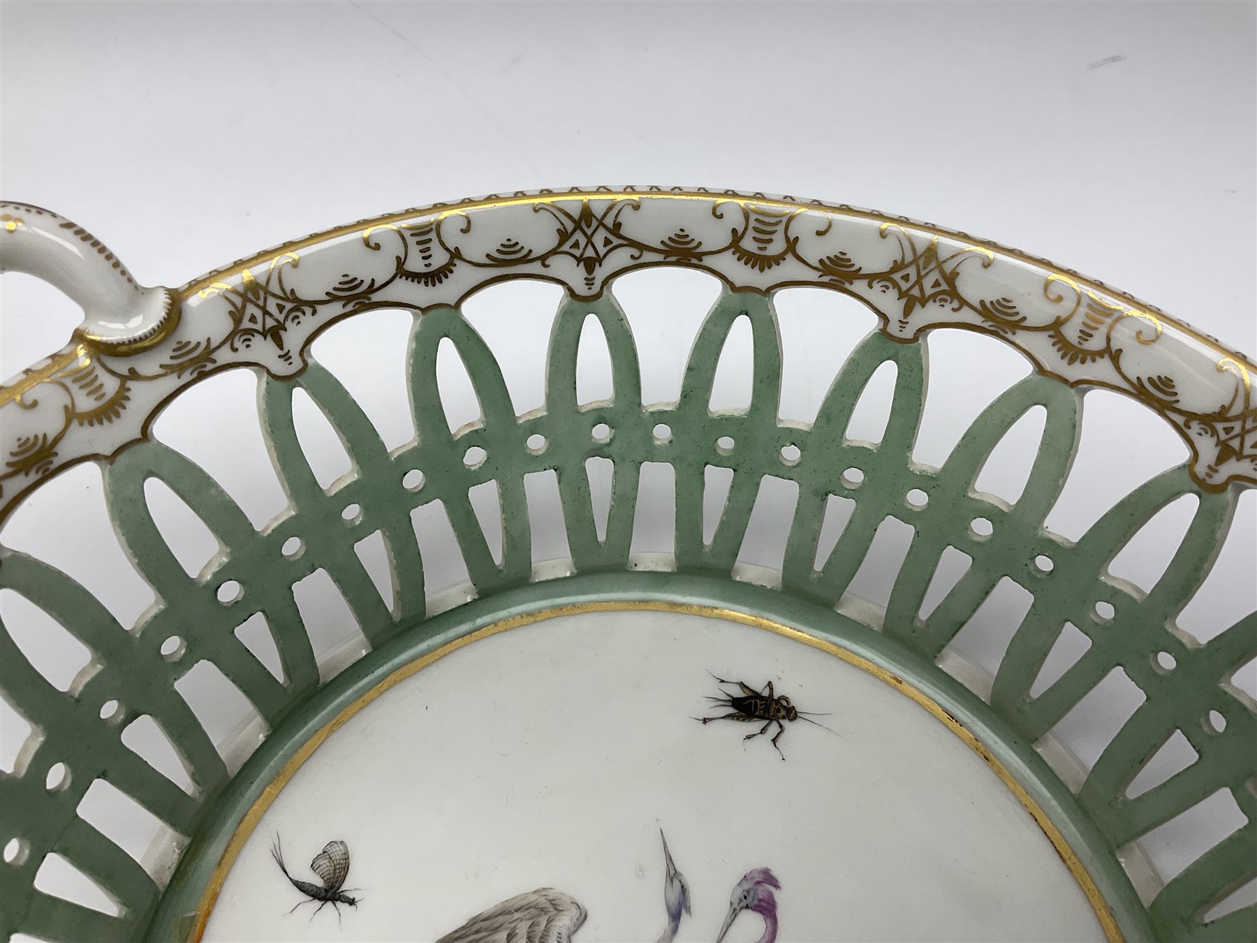 Pair of 19th century German openwork chestnut baskets, with twin handles and scrolling gilt border and star rim, painted to the centre with birds and insects, D22cm 