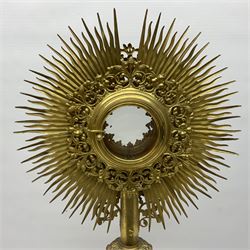 20th century gilt metal monstrance, in the Gothic revival style, with glazed aperture to centre surrounded with clear paste stones, in a pierced floral and scroll border set with coloured paste stones, within a sunburst surround, on a paste set knopped stem and similar foliate foot, H59.3cm