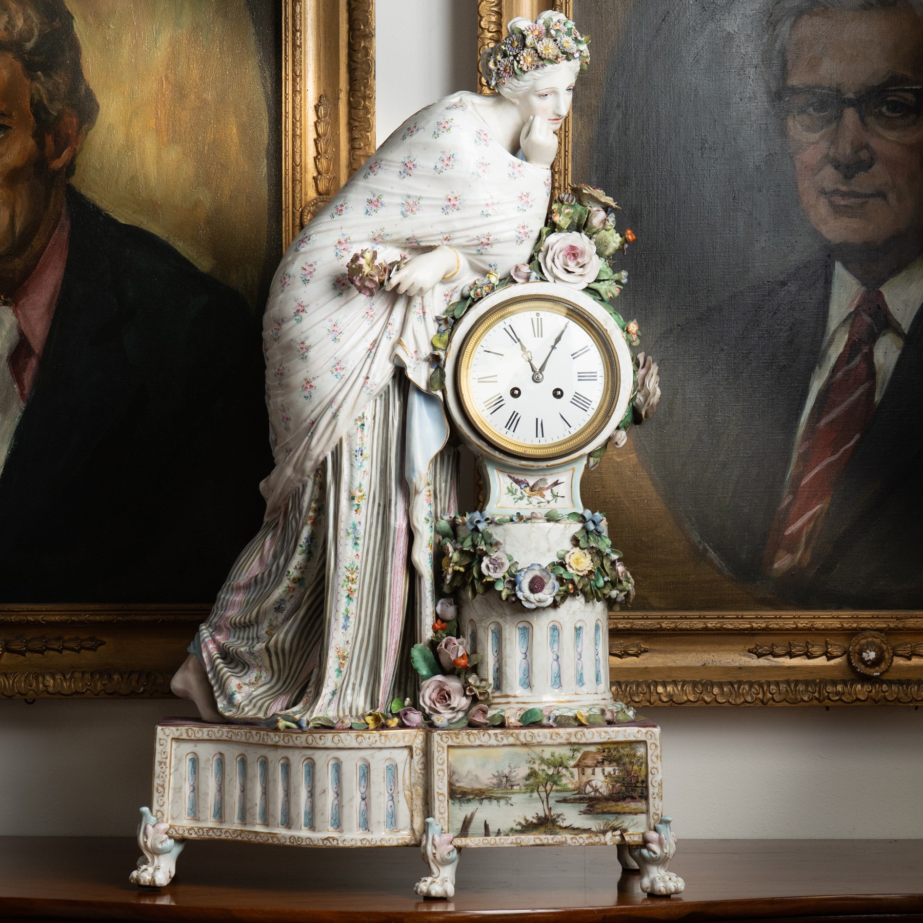 Large 19th century German porcelain mantel clock with white dial and striking movement, the case with a standing figure of Flora resting on a pillar with floral applied decoration, the base painted with landscape and floral panels on paw feet H77cm W43cm