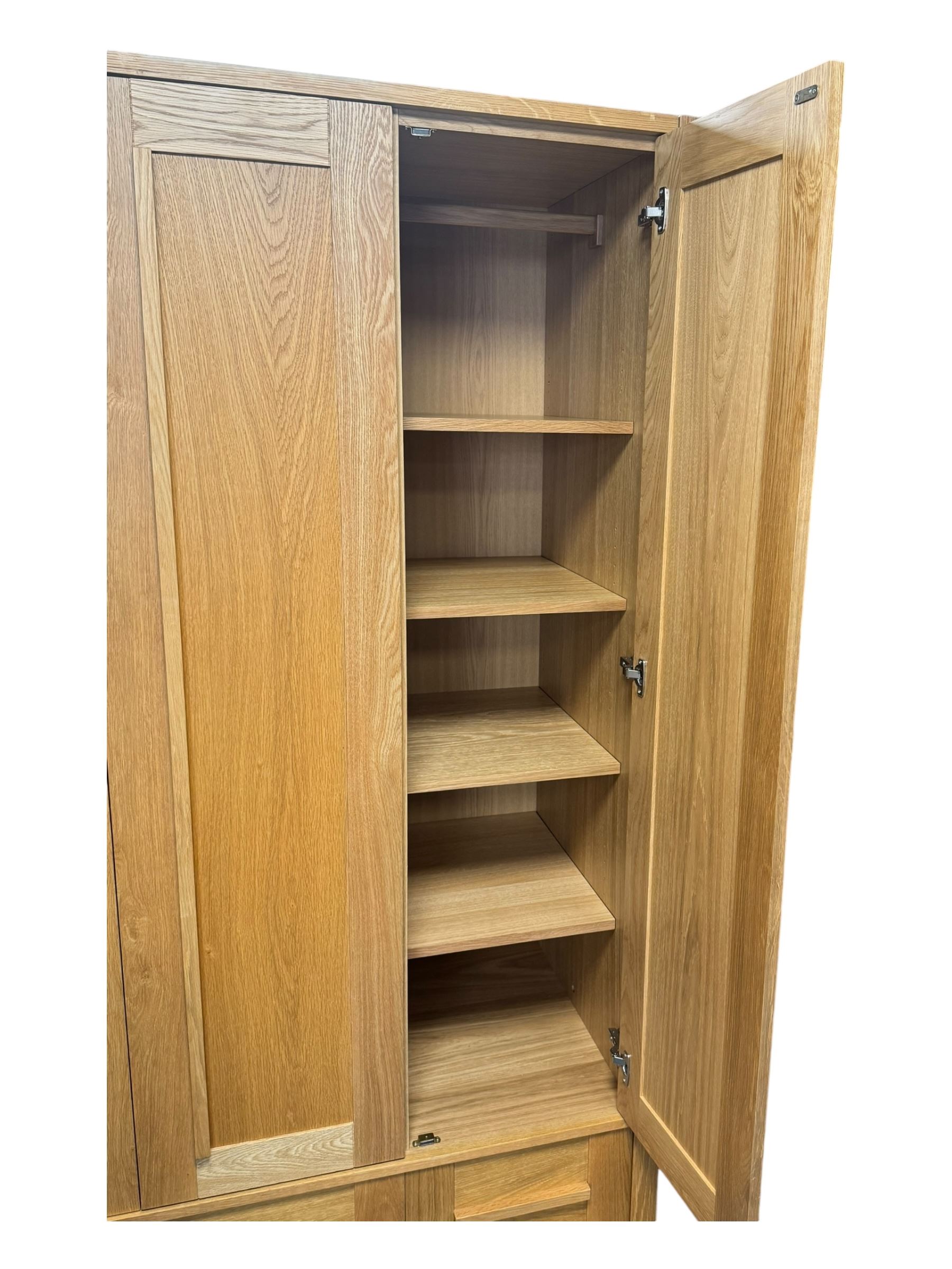 Contemporary light oak triple wardrobe, panelled doors with vertical linear design, left section enclosing hanging rail and single shelf, right section with adjustable shelves, over two drawers, on square stile supports