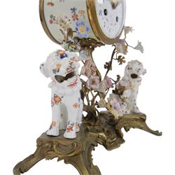 French- early 20th century 8-day Chinoiserie brass and porcelain mantel clock in the 18th century style, brass base with splayed feet profusely decorated with clusters of painted porcelain flowers and two decoratively painted Chinese foo dogs, movement enclosed in a circular porcelain movement case illustrated with birds of paradise and oriental motifs, with a white enamel dial Arabic numerals, minute markers, pierced gilt hands and a floral swag, rack striking Parisian movement striking the hours and half-hours on a bell. With a visible sunburst pendulum and key.