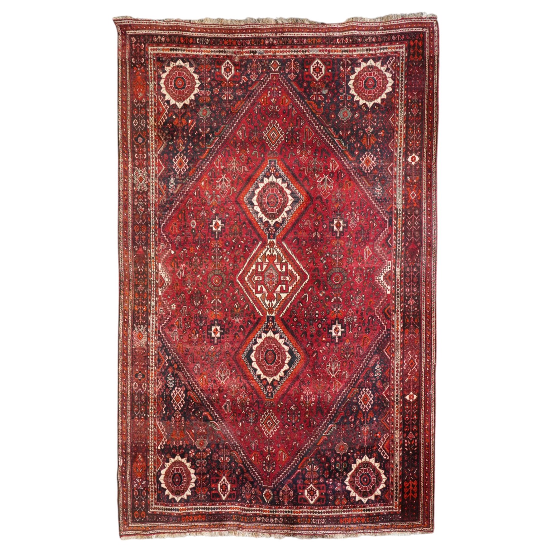 Large Persian Shiraz crimson ground carpet, the busy field decorated with a geometric pole medallion surrounded by stylised plant motifs with contrasting indigo spandrels and geometric-woven guard bands