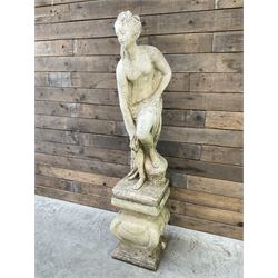 Cast stone garden statue of partially draped classical female figure on ornate pedestal 