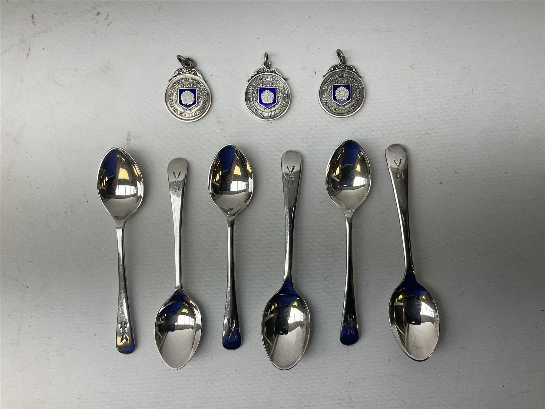 Set of three Yorkshire Miniature Rifle Association hallmarked silver and enamel fob medals, Birmingham 1925, 1926 & 1929; together with six silver plated coffee spoons each engraved with crossed rifles to the terminal (9)
