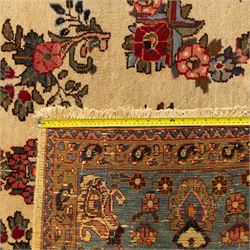 Central Persian Kashan hand-knotted carpet, cream ground, with a central lobbed floral burgundy, rose, and indigo medallion, surrounded by scrolling sprays of carnations and palmettes, with sky blue spandrels decorated with curvilinear vines and stylized blossoms, framed by a repeating terracotta border of palmettes, framed by narrow guard stripes 