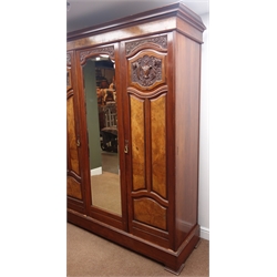  Edwardian walnut triple wardrobe, projecting cornice above two doors carved with urns and flowers, central door with full length bevel edge mirror, interior fitted with hanging rails and hook, three slides and three drawers, on shaped plinth base, W180cm, H212cm, D57cm  