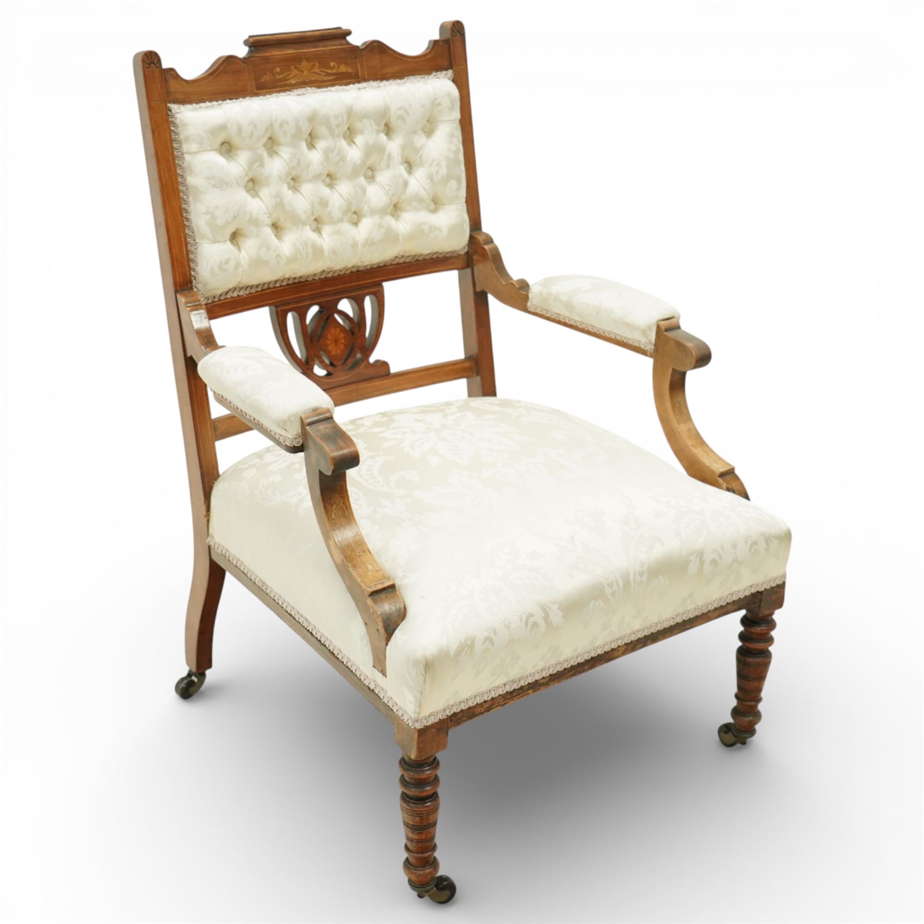 Edwardian mahogany open armchair, the upholstered rectangular back buttoned in ivory patterned fabric within a shaped top rail with inlaid foliate detail, open splat carved with a pierced anthemion motif centred by an inlaid roundel, swept open arms with upholstered pads, over a sprung upholstered seat, on turned front supports with brass castors