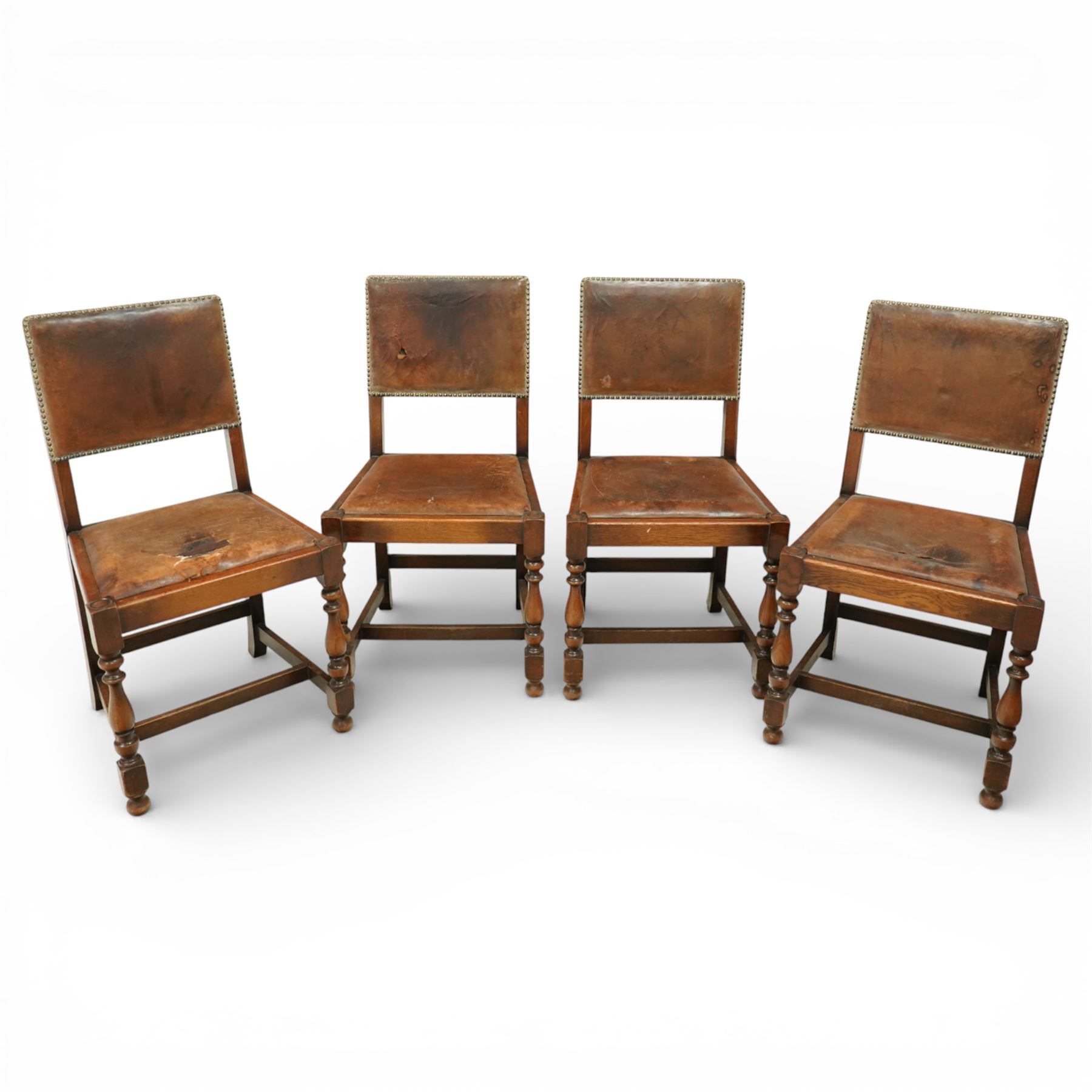 Early 20th century four oak side chairs, with studded leather upholstered backs and seats, on square section legs with baluster turned front supports and straight stretchers