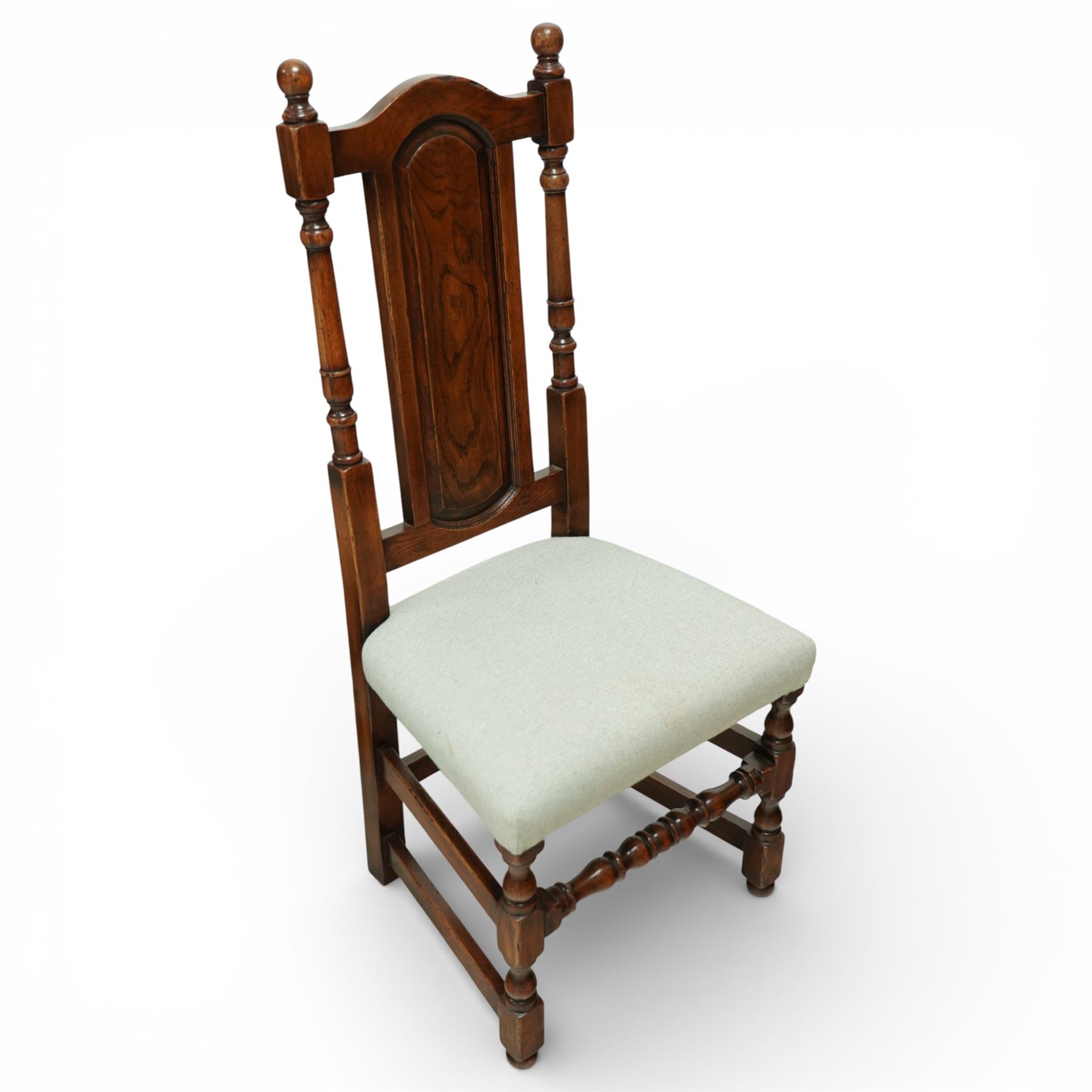 Country House oak high back dining chairs, set of ten comprising eight side chairs and two carvers, each with arched top rail flanked by turned finials over a central fielded panel back, with overstuffed seats upholstered in pale fabric, raised on turned front supports united by stretchers