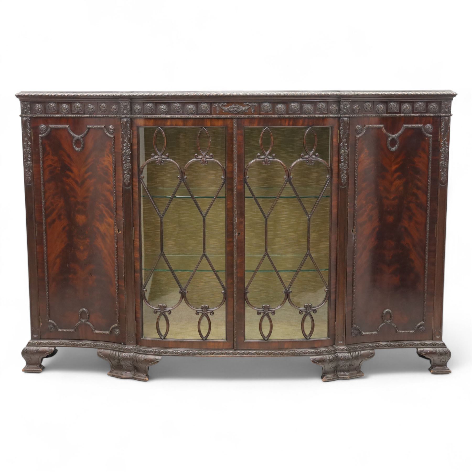 Edwardian mahogany serpentine breakfront display cabinet in the neoclassical style, the rectangular top above a carved frieze with roundels, foliage, and ribbon tied swags with central bow-fronted astragal glazed doors enclosing shelves, flanked by panelled doors, raised on bracket feet 