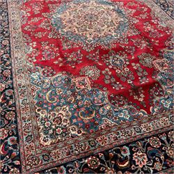 Meshed Persian rug, red, indigo, and teal background with repeating floral vine around a symmetrical floral medallion with bold palmettes, central ivory radiating floral centrepiece, and spandrels, indigo and teal border of delicate scrolling palmette and leafy floral vines