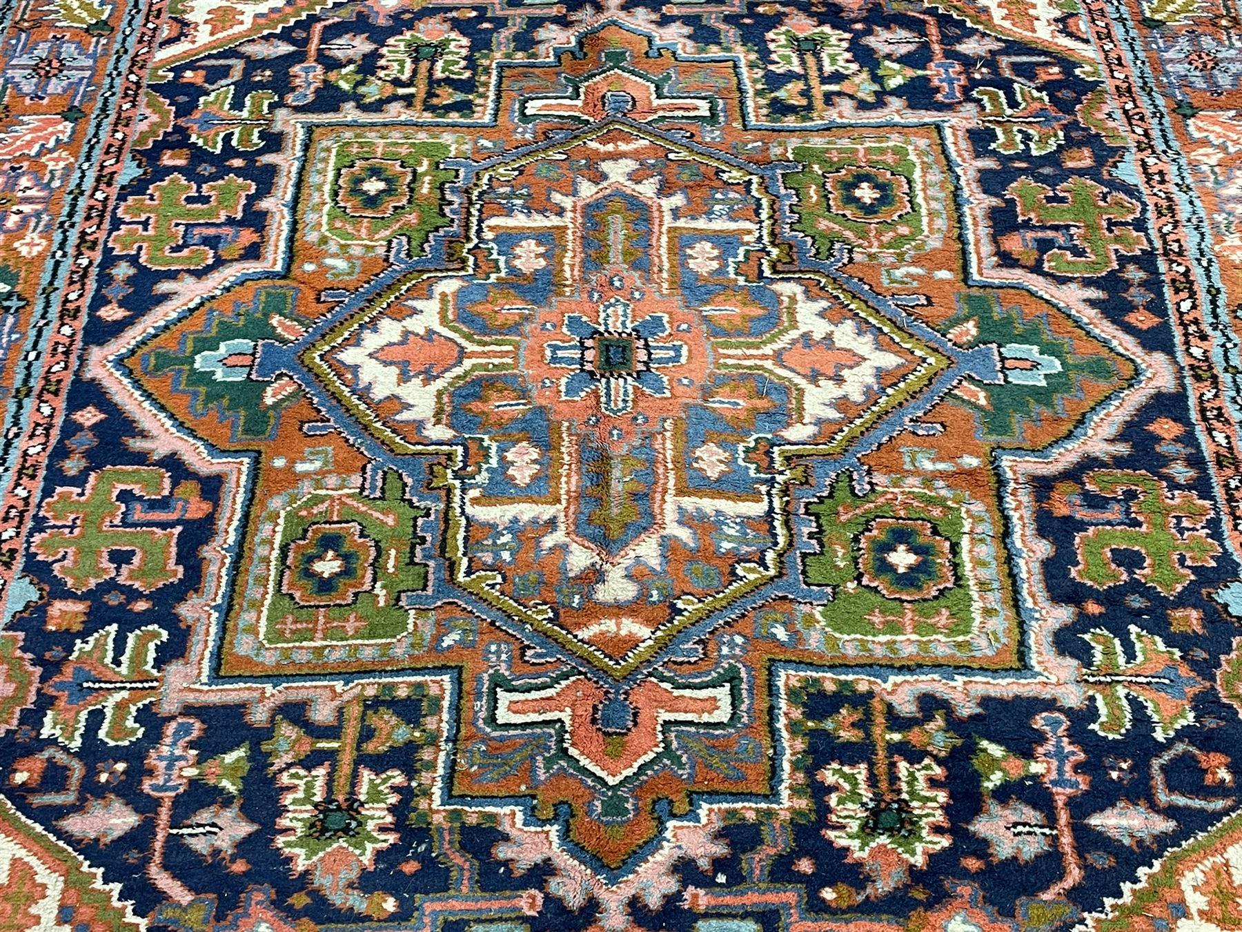 Persian Heriz indigo and rust ground rug, central geometric star medallion decorated with stylised foliate motifs, the border decorated with stylised flower heads
