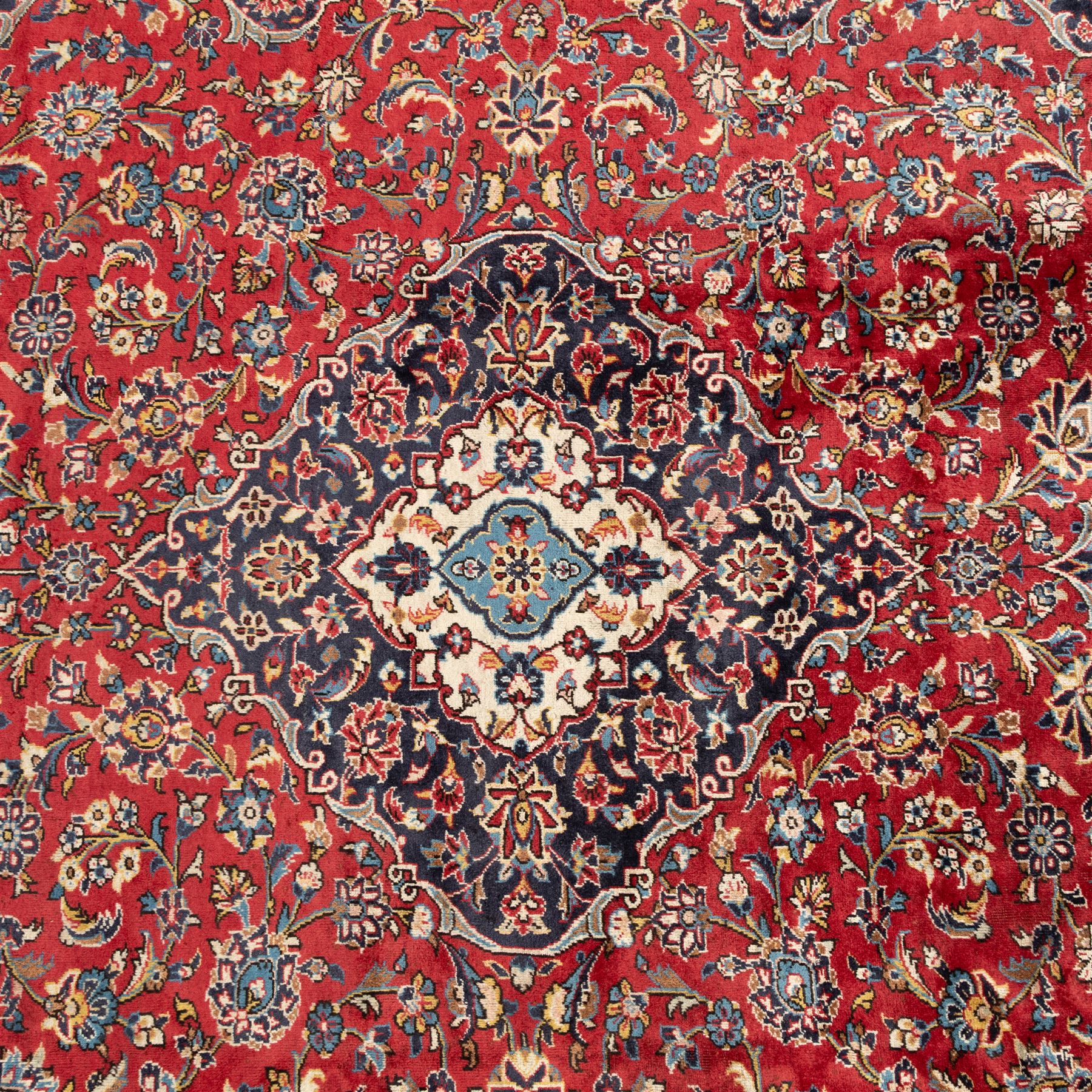 Persian Ardakan carpet, brick red field with ivory and navy central medallion, surrounded by stylised lotus blossoms and cloudband motifs, framed by rich indigo borders featuring palmettes, serrated leaves and angular vine work, woven in the city of Ardakan in central Iran