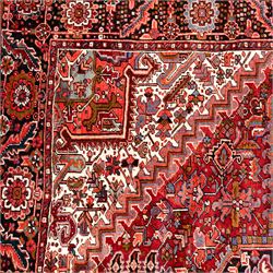 North West Persian Heriz hand-knotted carpet, brick red field, with large central angular star medallion with stepped outlines, surrounded by geometric floral devices and stylized rosettes, with corresponding corner spandrels, enclosed by a bold geometric main border with multiple guard stripes, with cotton fringe ends 