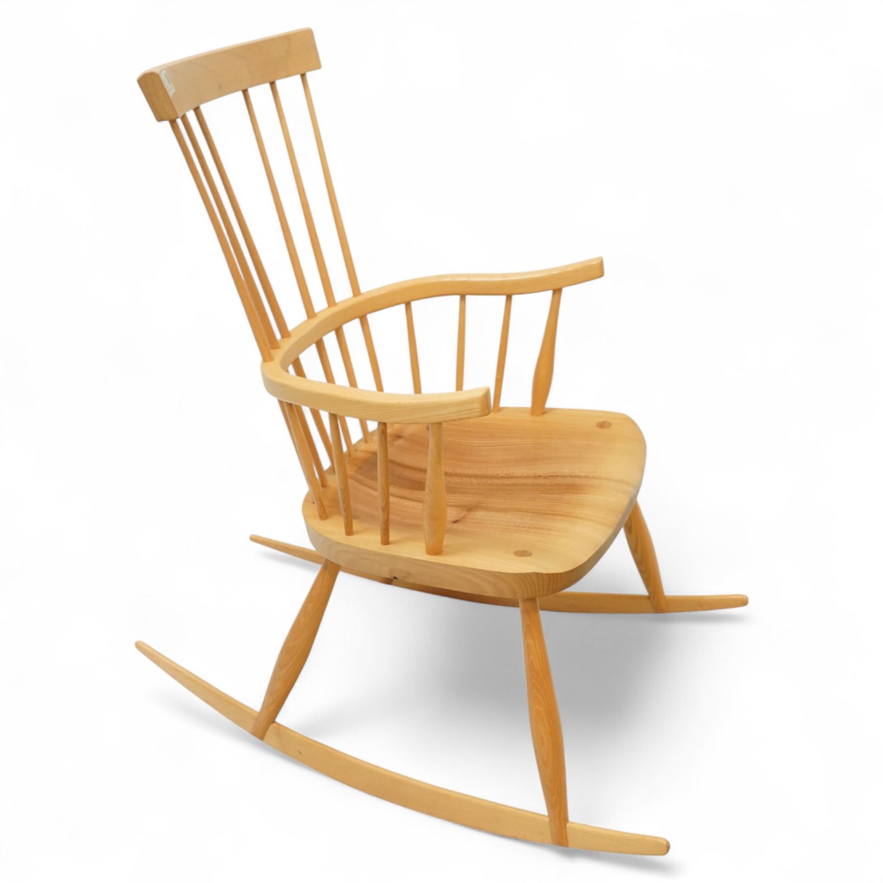 Mid 20th century Windsor ash rocking armchair, in the manner of Ercol, with curved cresting rail above nine stick spindles, shaped and chamfered paddle arms, figured shaped seat, raised on turned legs joined by twin side stretchers and mounted on curved rockers