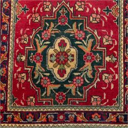 North West Persian Tabriz hand-knotted runner, madder red field with central octagonal medallions of sage green, navy and ivory, ground enclosing a floral rosette and radiating angular vinery, scrolling floral sprays and palmettes either end with shaped pendants principal border on navy ground decorated with a continuous vine-scroll of palmettes and rosettes, flanked by narrow guard borders, with cotton fringe ends 