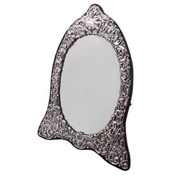 Modern silver mounted dressing table mirror of arched form, the oval bevelled mirror plate within a silver surround embossed with flower heads, and foliate and C scrolls, with navy blue velvet  back and easel style support verso, H32cm, hallmarked London 1990, makers mark WW
