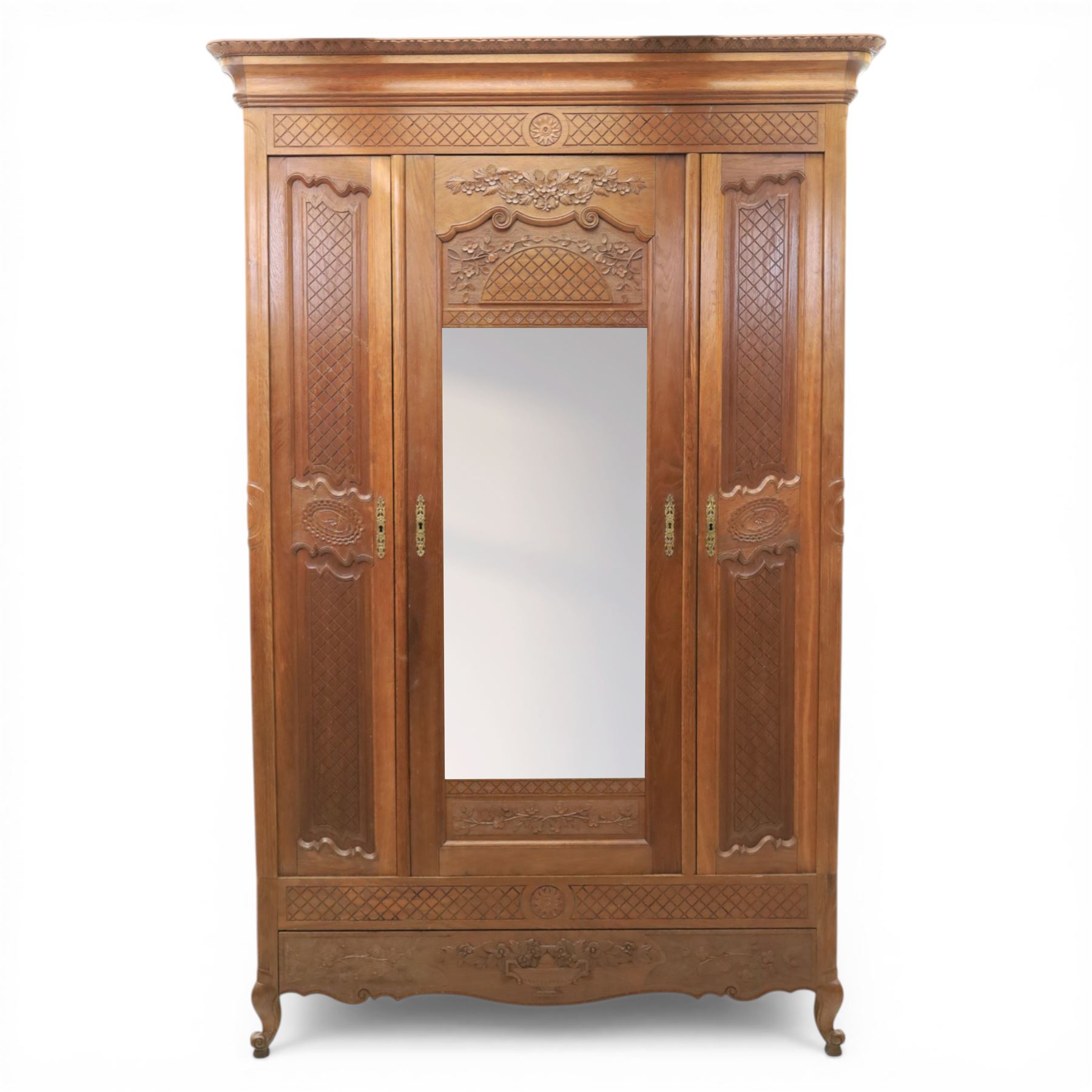 Early 20th century French oak triple door armoire, the moulded top above a frieze with carved lozenge decoration and central rosette, the central mirrored door enclosed by carved surround with floral crest, flanked by panelled doors with lattice carving, the base with shaped apron centred by carved basket motif, upon shaped cabriole supports