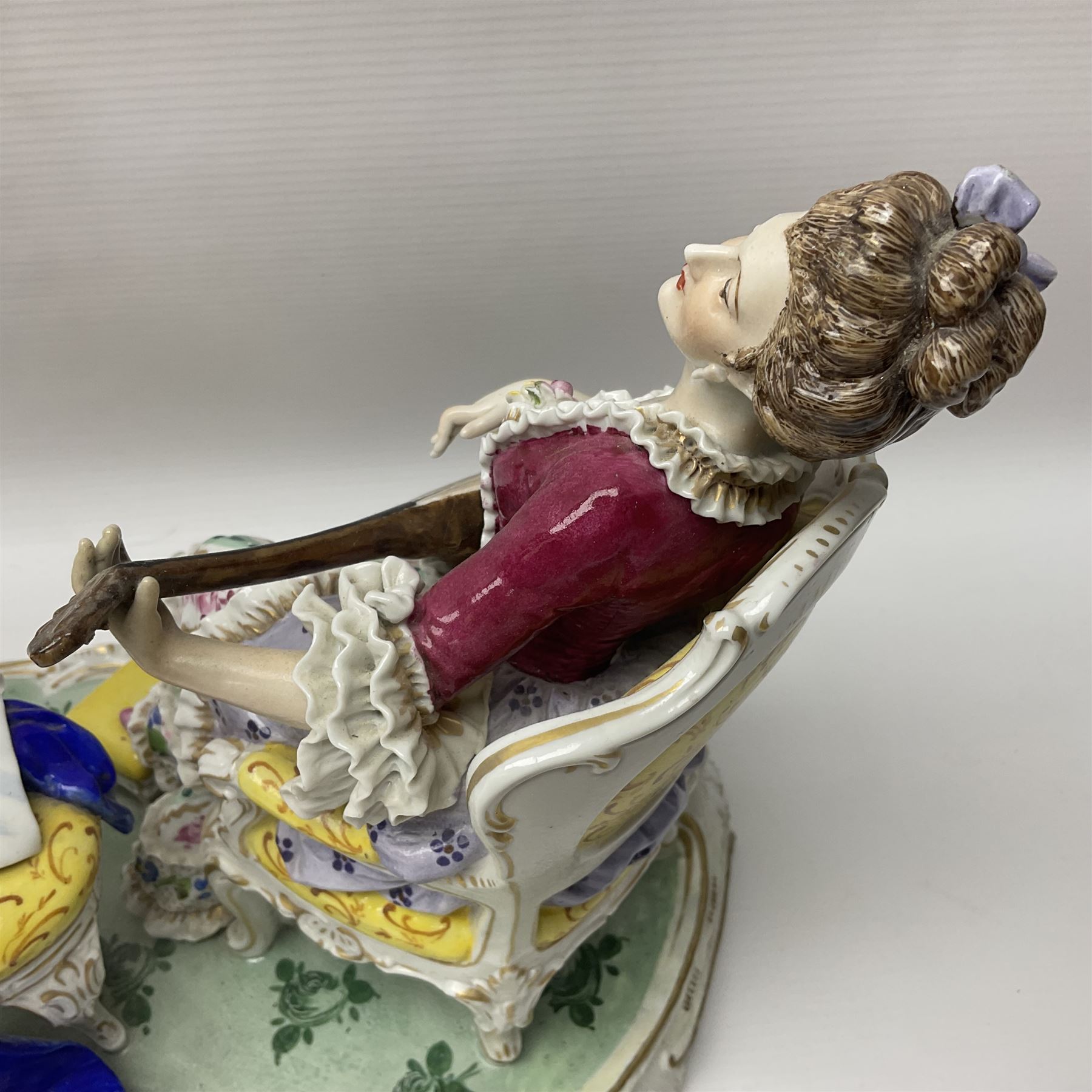 20th century Naples figure group, modelled as a seated female figure playing the lute seated, before a male figure stood holding a sheet of music, each in period dress, upon an oval base with gilt heightened scroll edge, with crowned N mark beneath, H31.5cm L33cm
