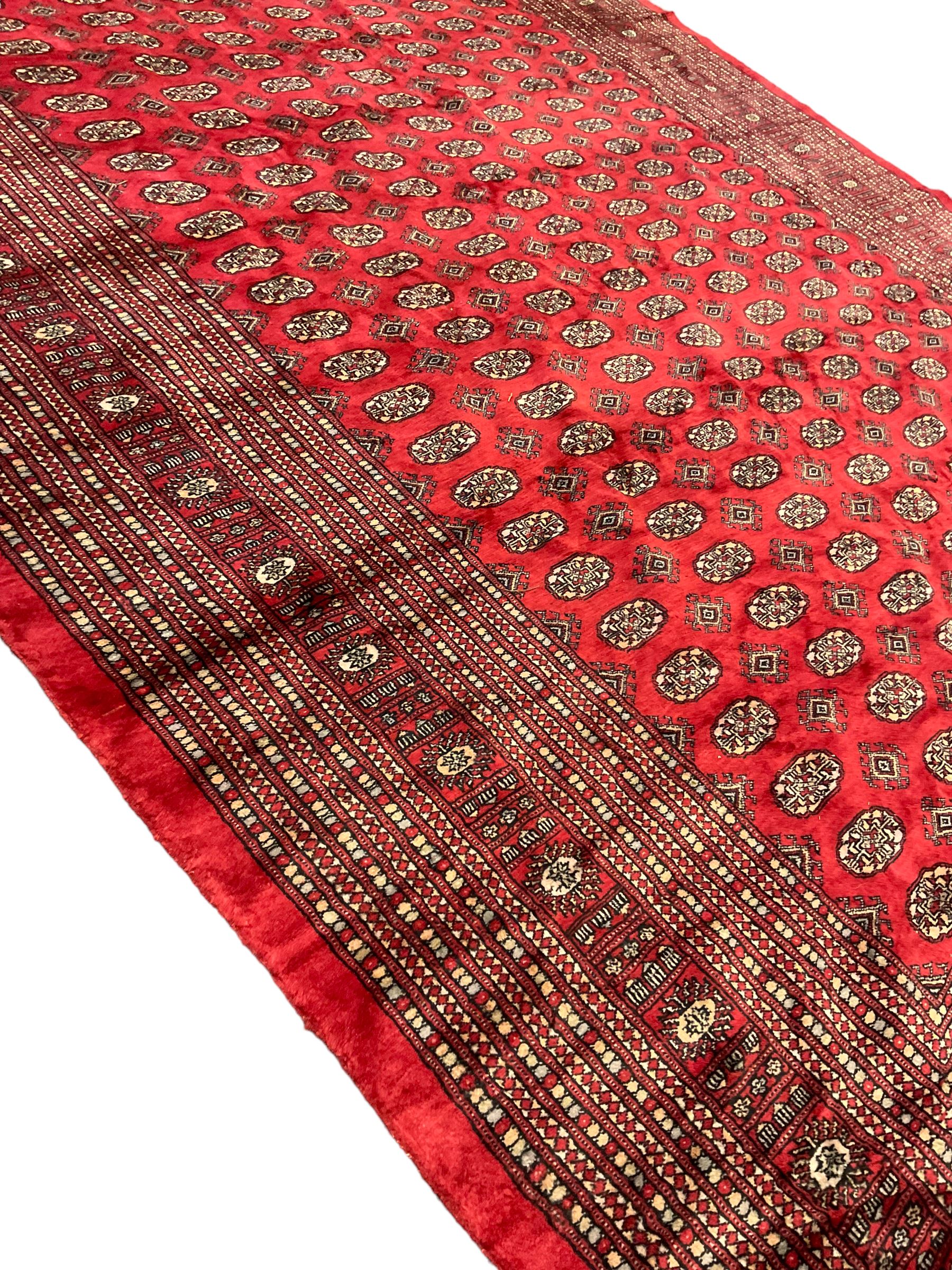 Persian Bokhara crimson ground carpet, the field decorated with repeating Gul motifs and lozenges, the multi-band geometric border with stylised plant motifs, two additional bands at the ends with geometric lozenges