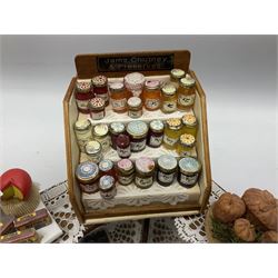 Collection of miniature dolls house grocery shop furniture and produce, comprising glazed corner counter with brass style cash register, shelved preserves unit, pies, cheese board and trays of meats, pair of white cheese counters, biscuit display with six tins, glazed preserves cabinet, pair of shop chairs and four further cheese boards complete with grapes and label flags