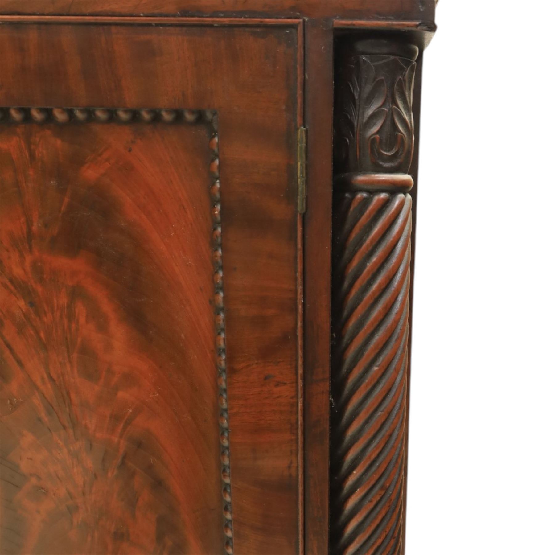  Pair of Regency mahogany bedside cabinets, rectangular top above a central cupboard door with flame mahogany veneer, flanked by spirally turned column uprights, raised on shaped supports