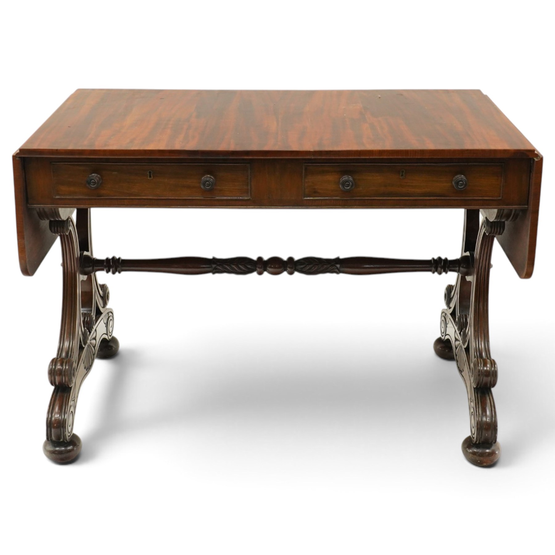 Fine 19th century figured mahogany sofa table, the rectangular twin drop-leaf top with rounded corners above two cock-beaded frieze drawers with opposing faux drawers, fitted with turned handles, raised on twin reeded and C-scroll-carved end supports with palmette-carved platform bases and compressed bun feet, united by a turned and foliate-carved stretcher