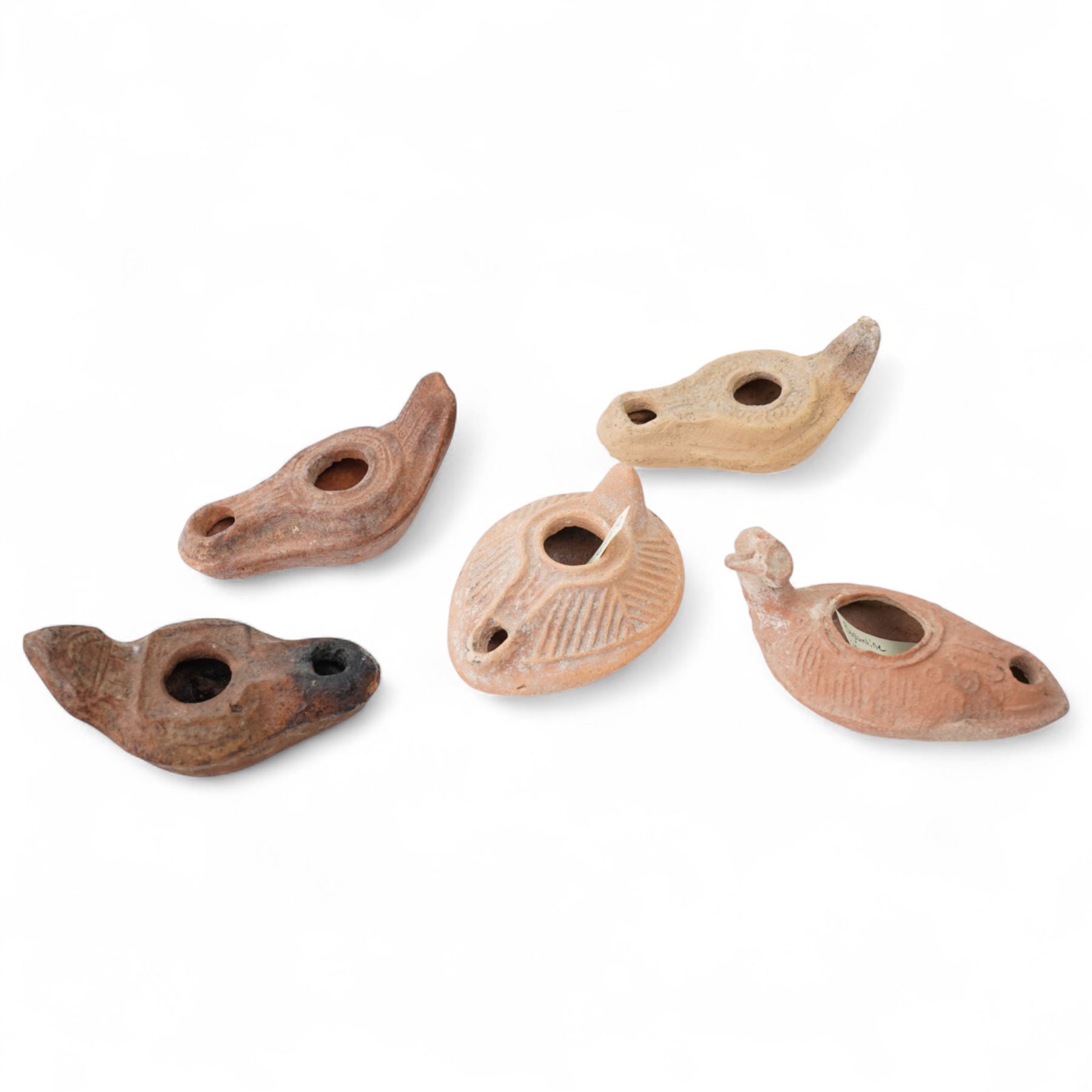 A group of four Byzantine terracotta oil lamps - Eastern Mediterranean, c.5th-7th century AD, comprising a group of mould-made slipper-form oil lamps, each with a rounded body, large central filling hole, and a short to elongated nozzle; including one with fine radiating linear decoration, and another preserving ancient use with traces of oil and wick residue within the burnished interior; together with a Crusader-period terracotta oil lamp (c.12th-13th century AD) of angular form with recessed panel decoration and a pierced handle moulded as a stylised animal head
Provenance: By the vendor’s repute, acquired/collected in the Middle East (Dead Sea area/Syria) in the 1960s